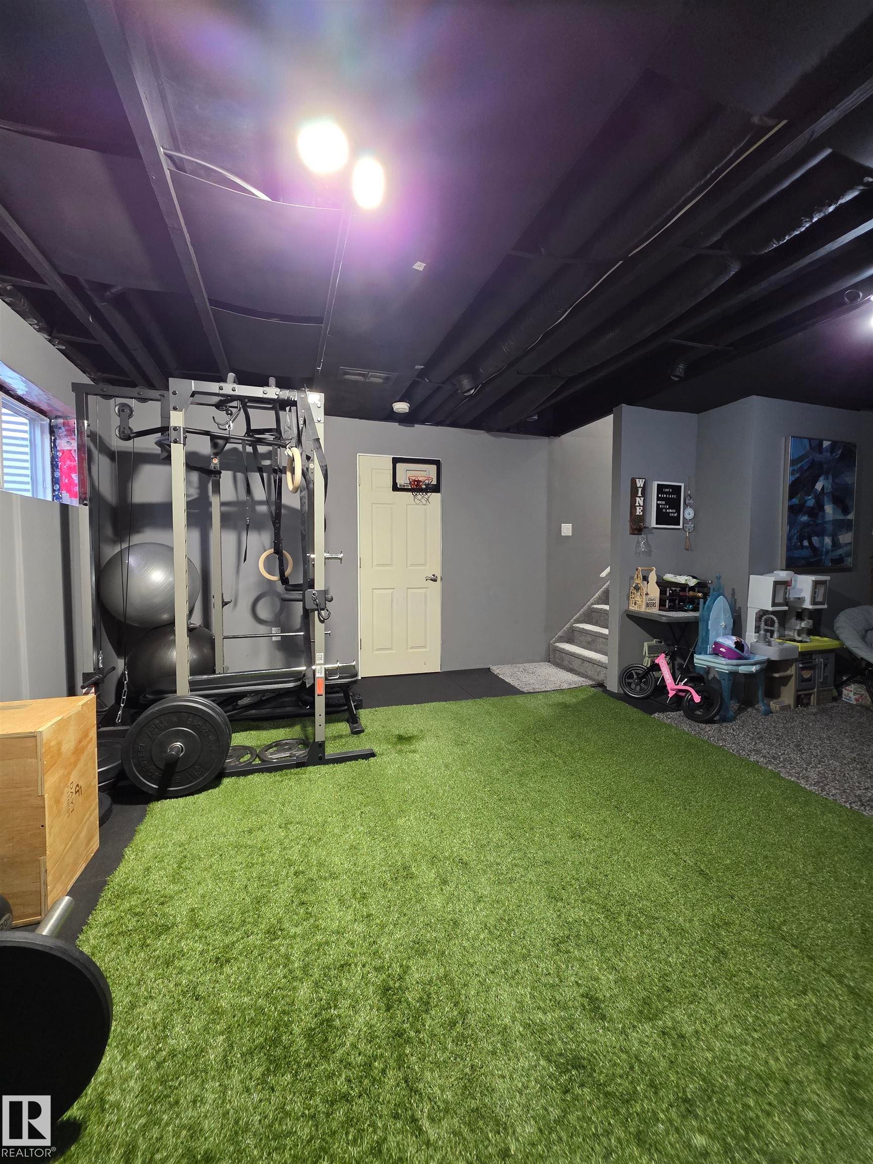Versatile lower-level space featuring a turf floor area and dedicated exercise equipment zone - 491 Ebbers Way, Edmonton, AB