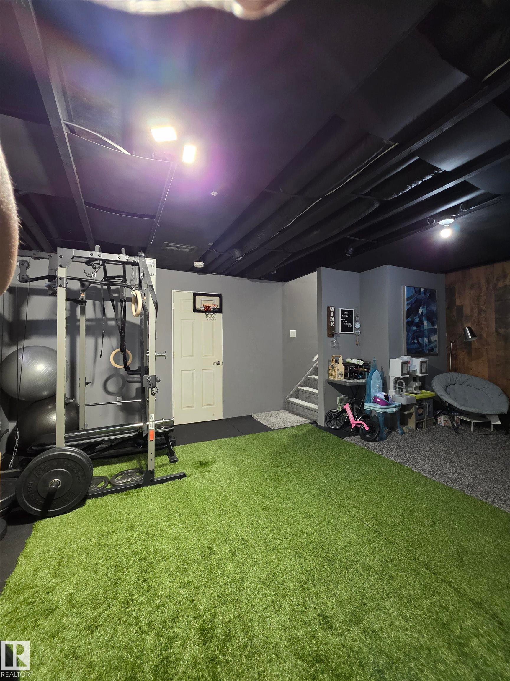 Recreational space featuring artificial turf flooring, painted exposed ceiling joists, and a partial wood-paneled wall - 491 Ebbers Way, Edmonton, AB