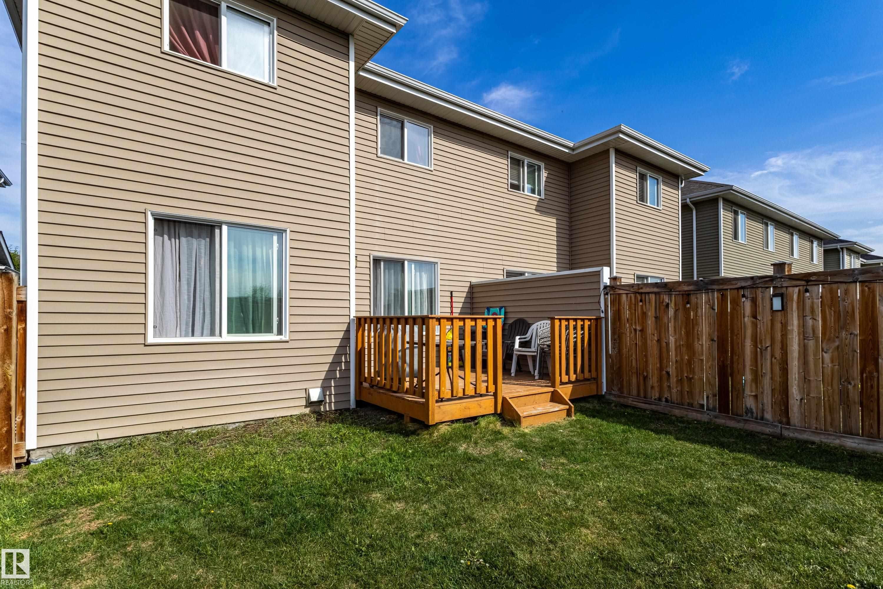 Rear exterior featuring a wooden deck with railing, a grass lawn, and a wood privacy fence - 491 Ebbers Way, Edmonton, AB