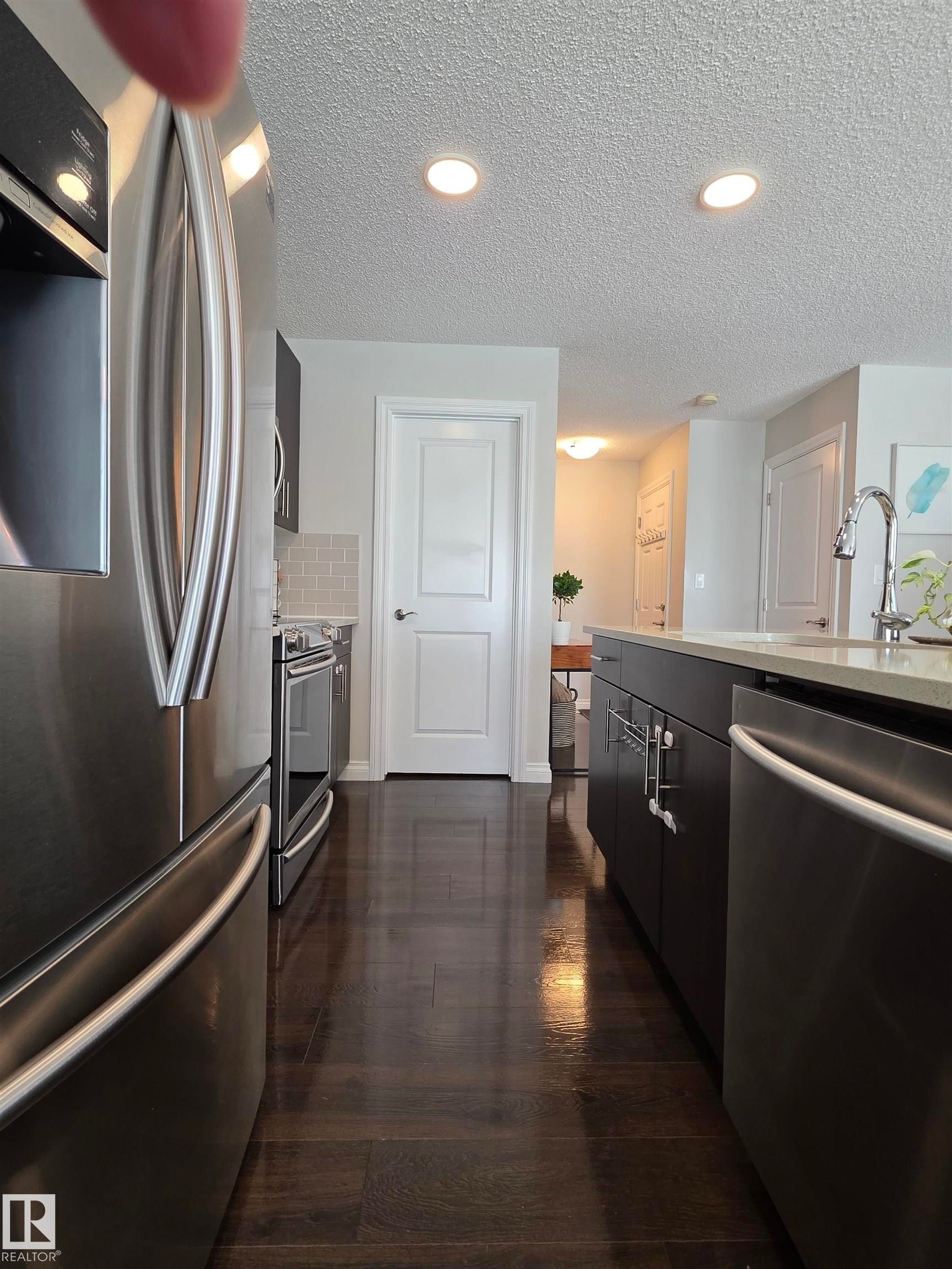 Kitchen featuring wood-finish flooring, stainless steel appliances, dark cabinetry, light countertops, and recessed lighting - 491 Ebbers Way, Edmonton, AB