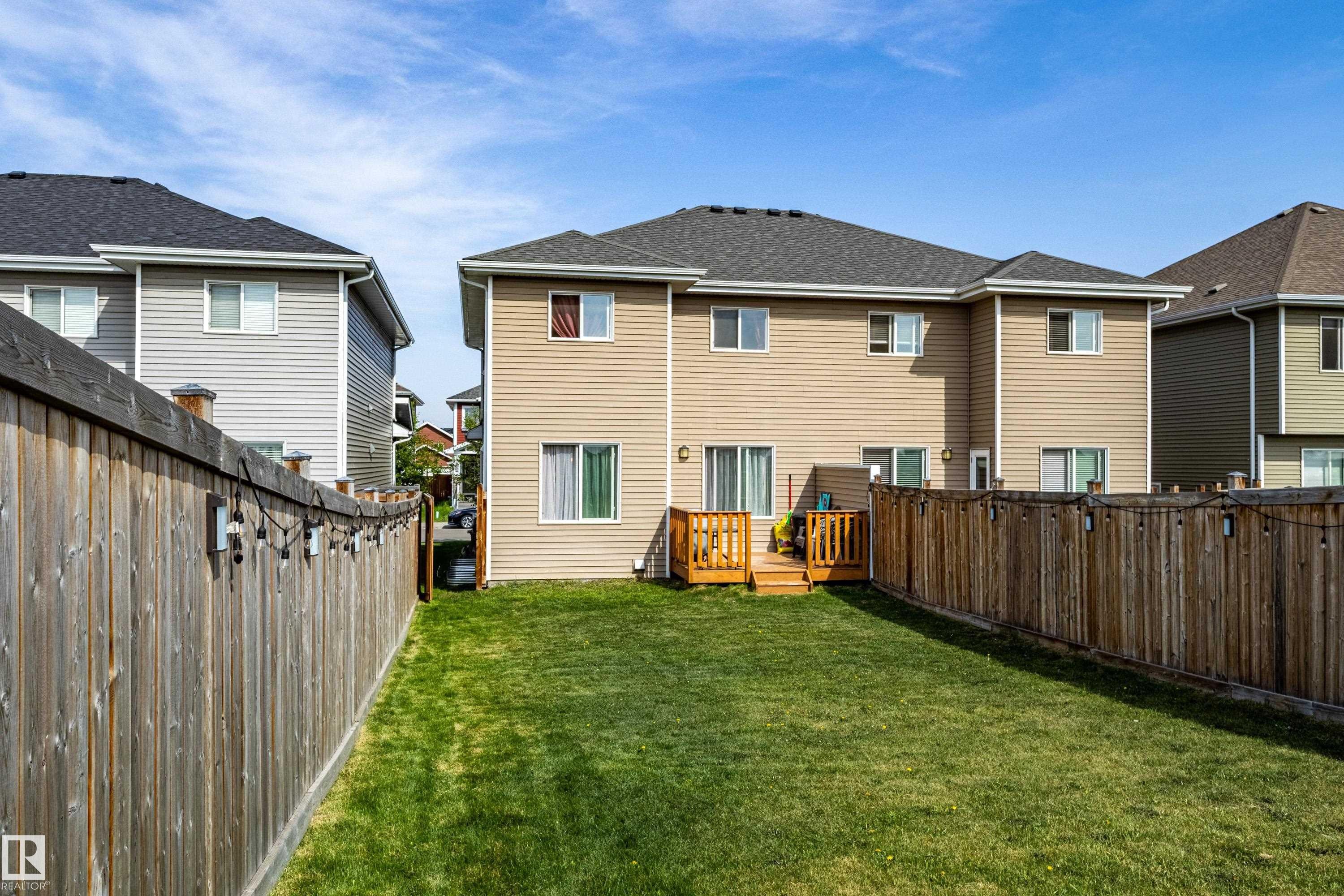 Expansive grass yard bordered by a privacy fence, featuring a raised wood deck with railings, and a tan siding exterior with multiple windows and sliding patio doors - 491 Ebbers Way, Edmonton, AB