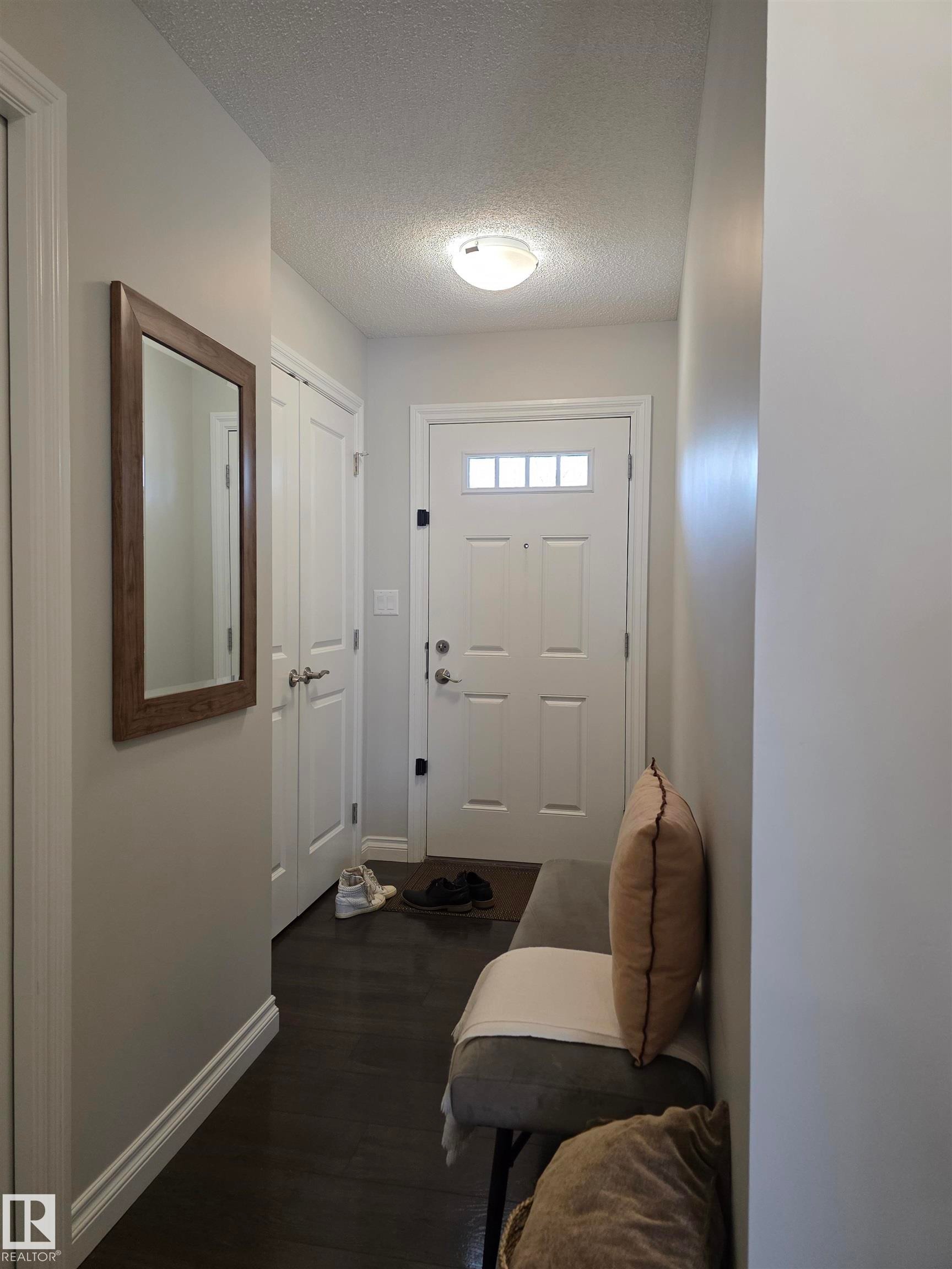 Entryway featuring a white paneled door with glass inserts, dark wood-finish flooring, and light gray painted walls - 491 Ebbers Way, Edmonton, AB