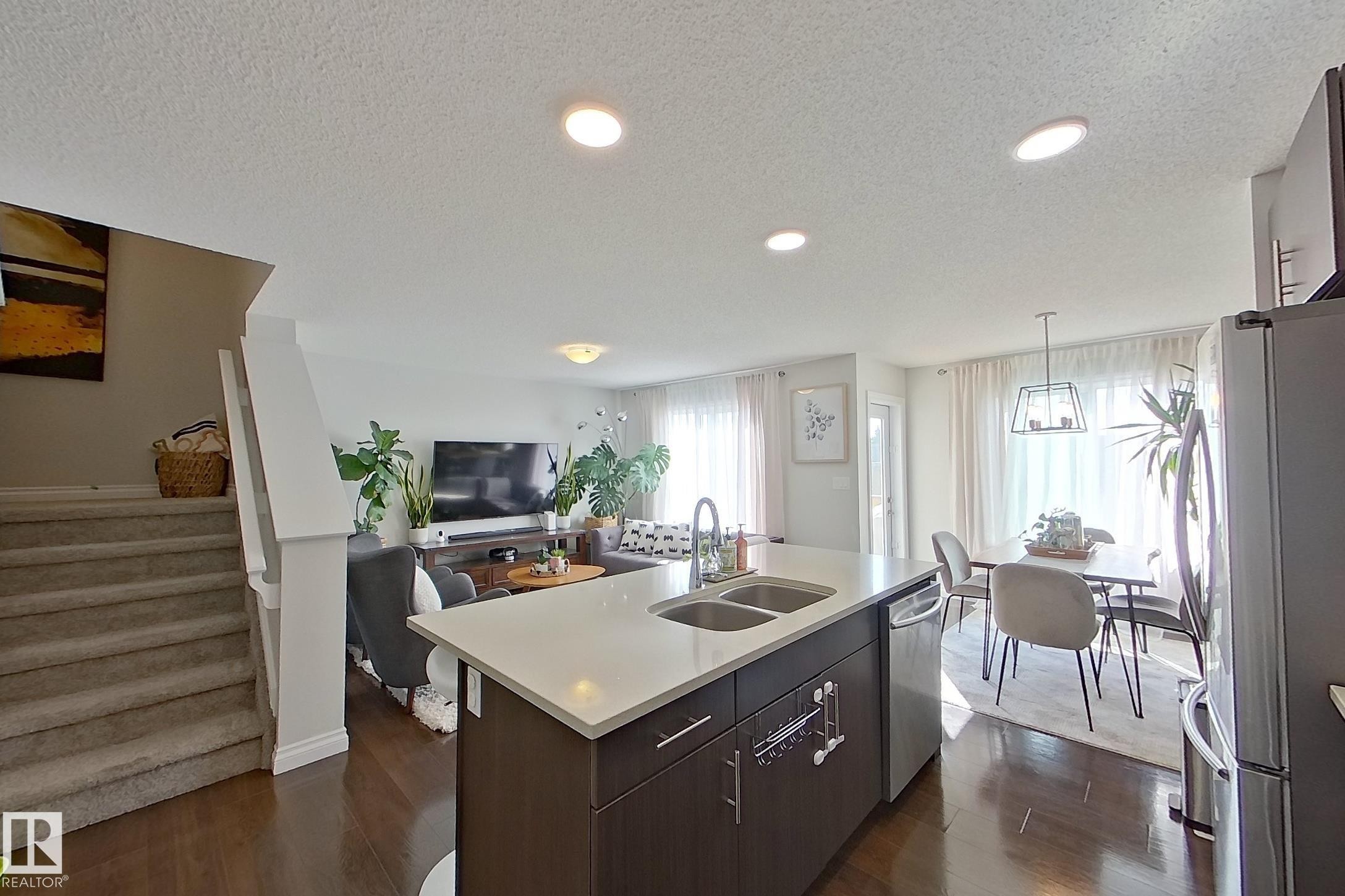 Kitchen island featuring a double-basin stainless steel sink with a high-arc faucet, light-colored countertop, and dark wood-finish cabinetry - 491 Ebbers Way, Edmonton, AB