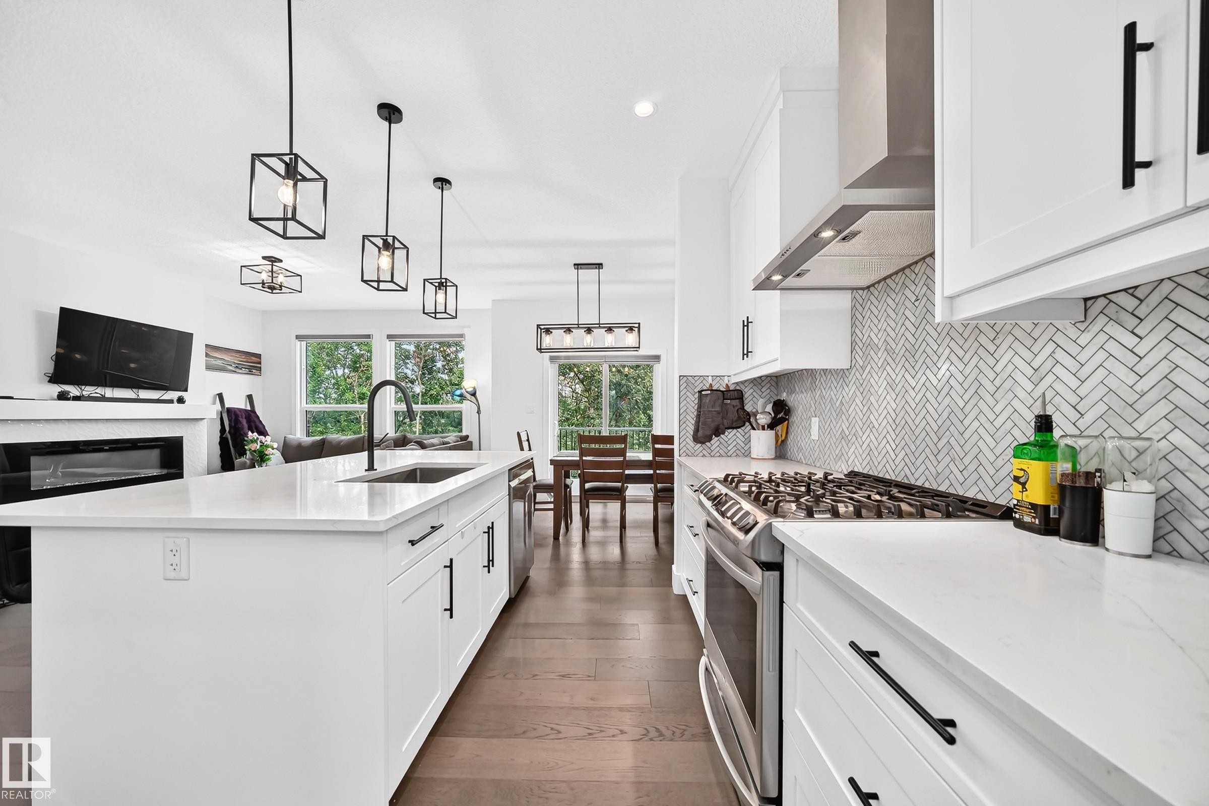 Contemporary kitchen featuring a large center island with integrated sink, white cabinetry with matte black hardware, stainless steel gas range, and a herringbone pattern tile backsplash - 22270 99A Avenue Nw, Edmonton, AB - Indoor Photo Showing Kitchen With Upgraded Kitchen