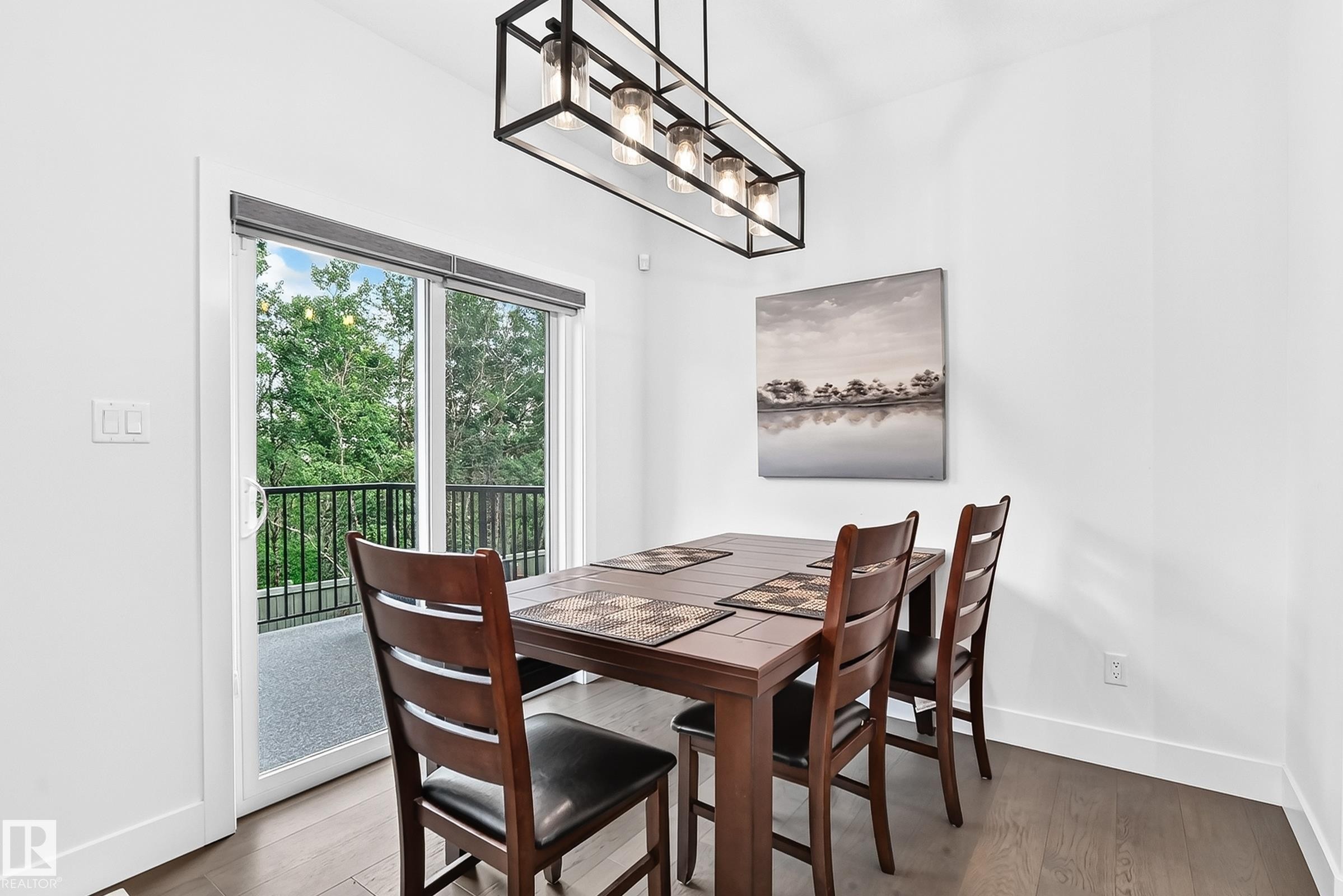 Dining area featuring a contemporary linear chandelier, wood-finish flooring, and crisp white walls - 22270 99A Avenue Nw, Edmonton, AB - Indoor Photo Showing Dining Room