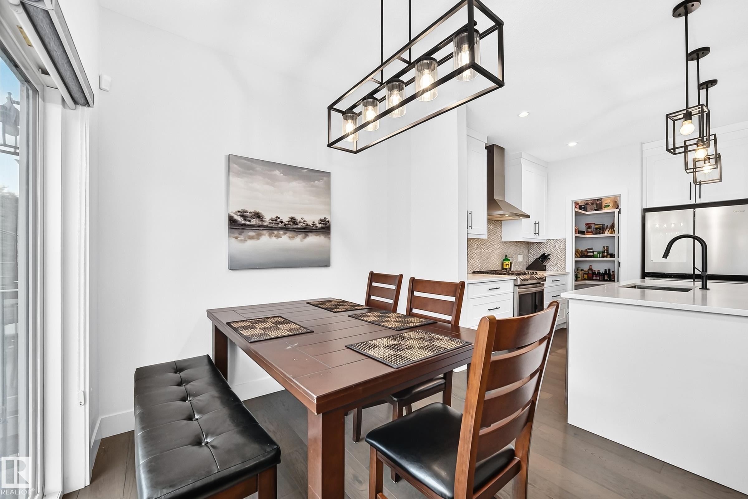 Modern kitchen and dining area featuring white cabinetry, stainless steel appliances, and a kitchen island with seating - 22270 99A Avenue Nw, Edmonton, AB - Indoor