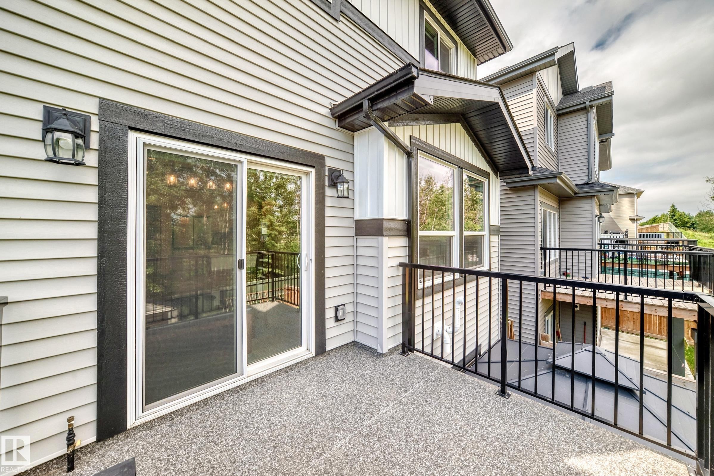 Private outdoor deck featuring a textured aggregate surface, black metal railings, and a sliding glass door entry - 22270 99A Avenue Nw, Edmonton, AB - Outdoor With Exterior