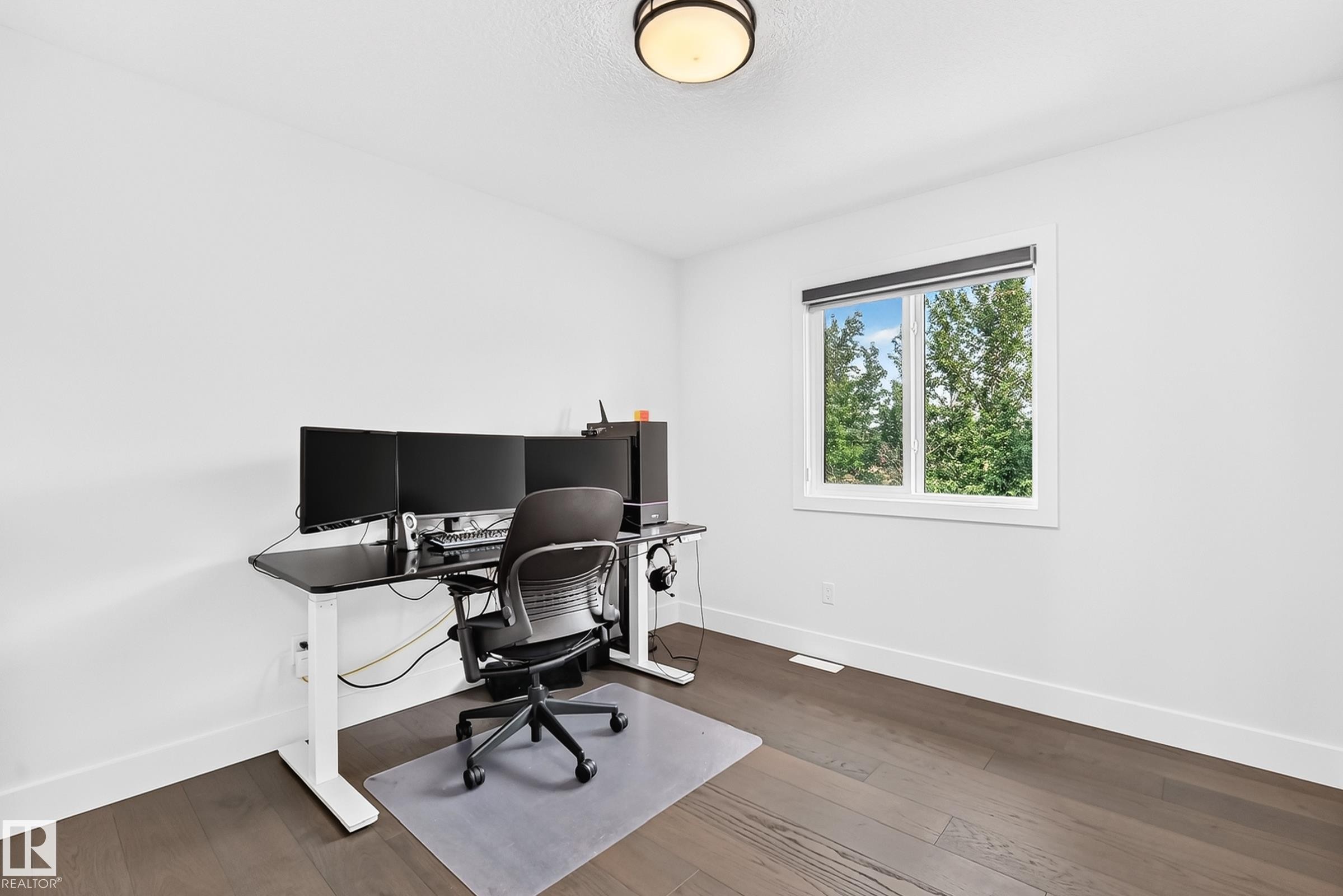 Bright room featuring a prominent window, dark wood-finish flooring, white walls, white baseboards, and a flush-mount ceiling light fixture - 22270 99A Avenue Nw, Edmonton, AB - Indoor Photo Showing Office