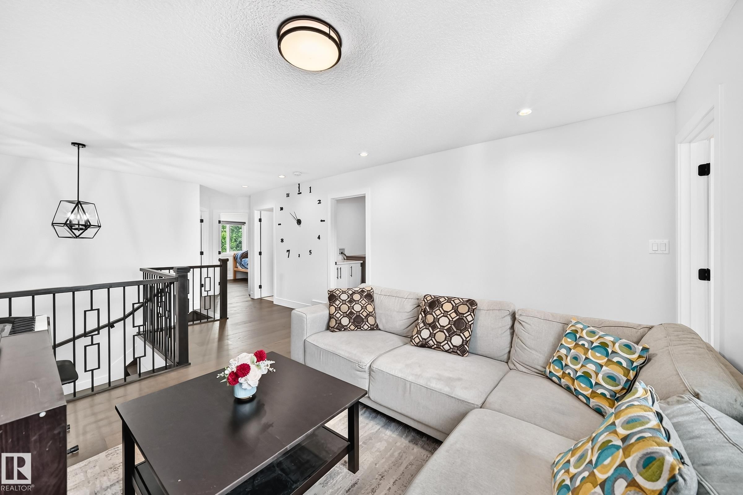 Lounge area featuring wood-finish flooring, a contemporary black metal stair railing, and a modern geometric pendant light fixture - 22270 99A Avenue Nw, Edmonton, AB - Indoor Photo Showing Living Room