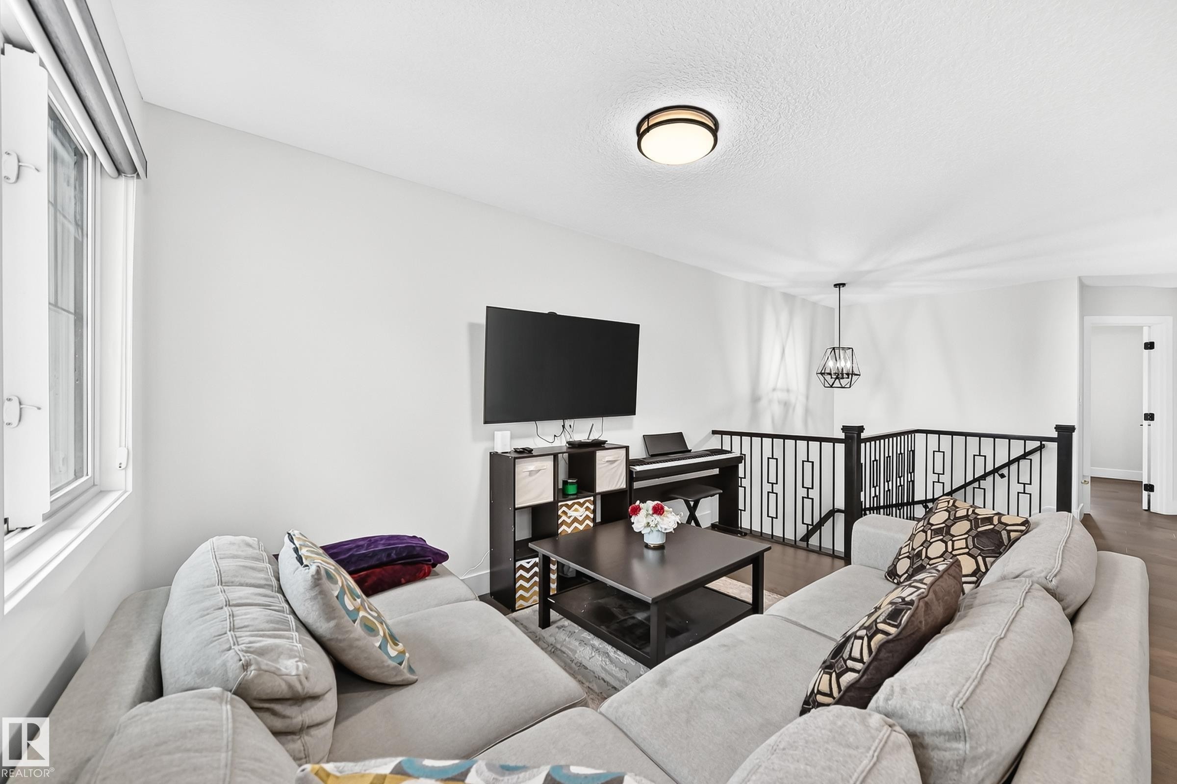 Open concept living area featuring wood-finish flooring, a contemporary black metal stair railing, and a window with blinds - 22270 99A Avenue Nw, Edmonton, AB - Indoor Photo Showing Living Room