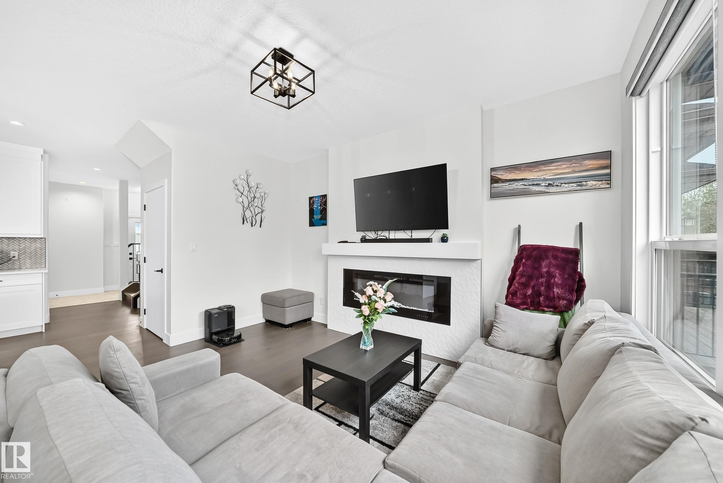Living area featuring a contemporary linear fireplace with a textured tile surround, dark wood-finish flooring, and crisp white walls - 22270 99A Avenue Nw, Edmonton, AB - Indoor Photo Showing Living Room With Fireplace