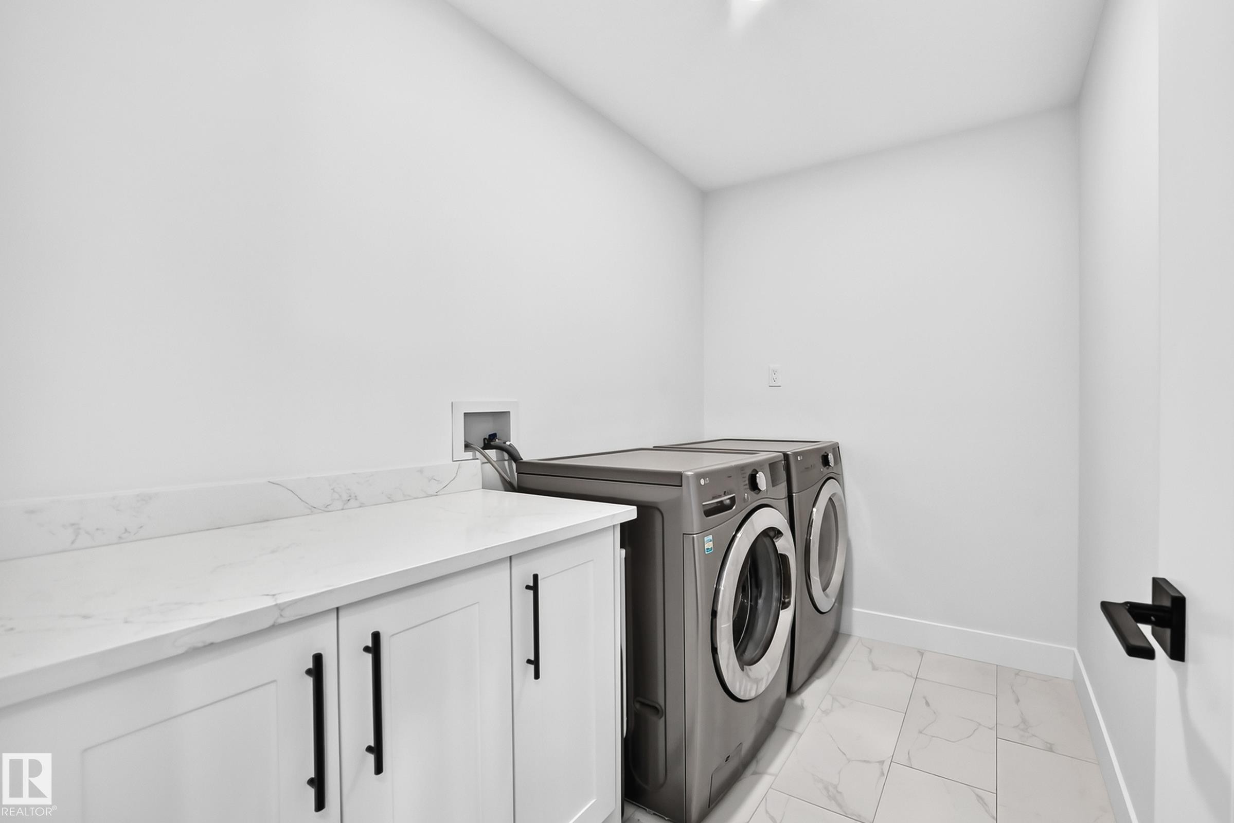 Laundry area featuring a built-in white countertop with an integrated backsplash, white cabinetry with black bar pulls, and tile flooring - 22270 99A Avenue Nw, Edmonton, AB - Indoor Photo Showing Laundry Room