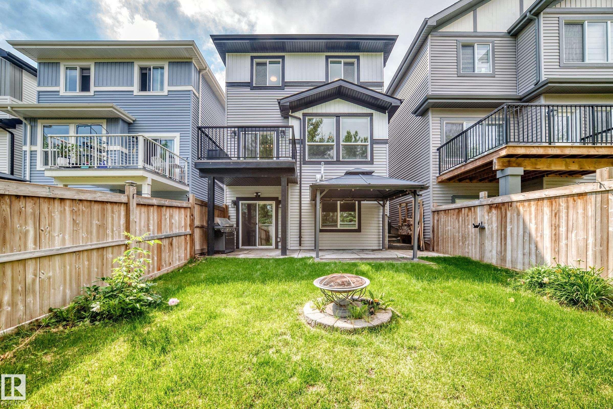 Expansive backyard featuring a manicured lawn, full fencing, an upper-level deck with black railing, a ground-level covered patio, and a lower-level glass sliding door entry - 22270 99A Avenue Nw, Edmonton, AB - Outdoor