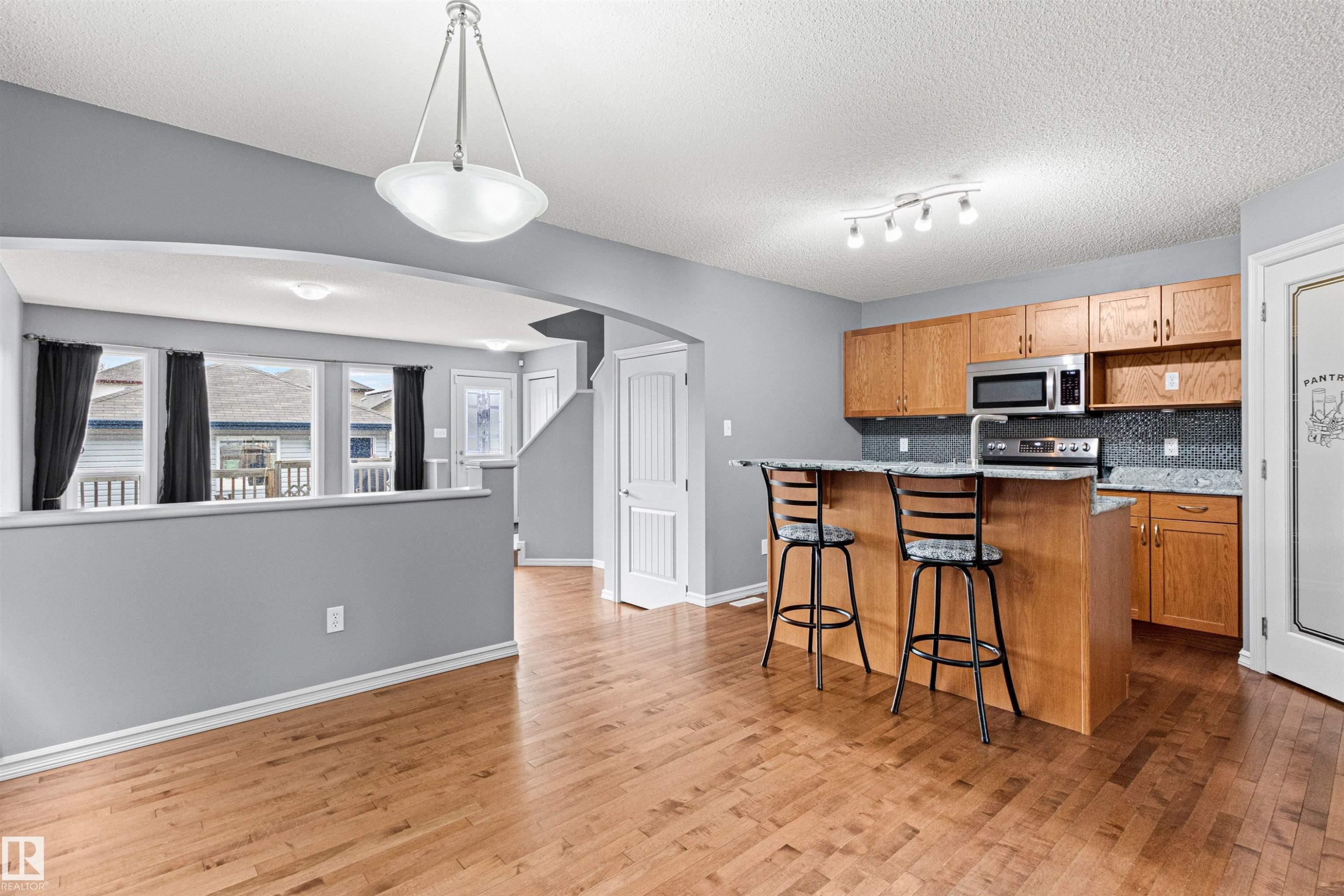 Open-concept kitchen and dining area featuring wood-finish flooring, a kitchen island with seating, natural wood cabinetry, stainless steel appliances, and a tiled backsplash - 1154 35A Avenue Nw, Edmonton, AB - Indoor Photo Showing Kitchen