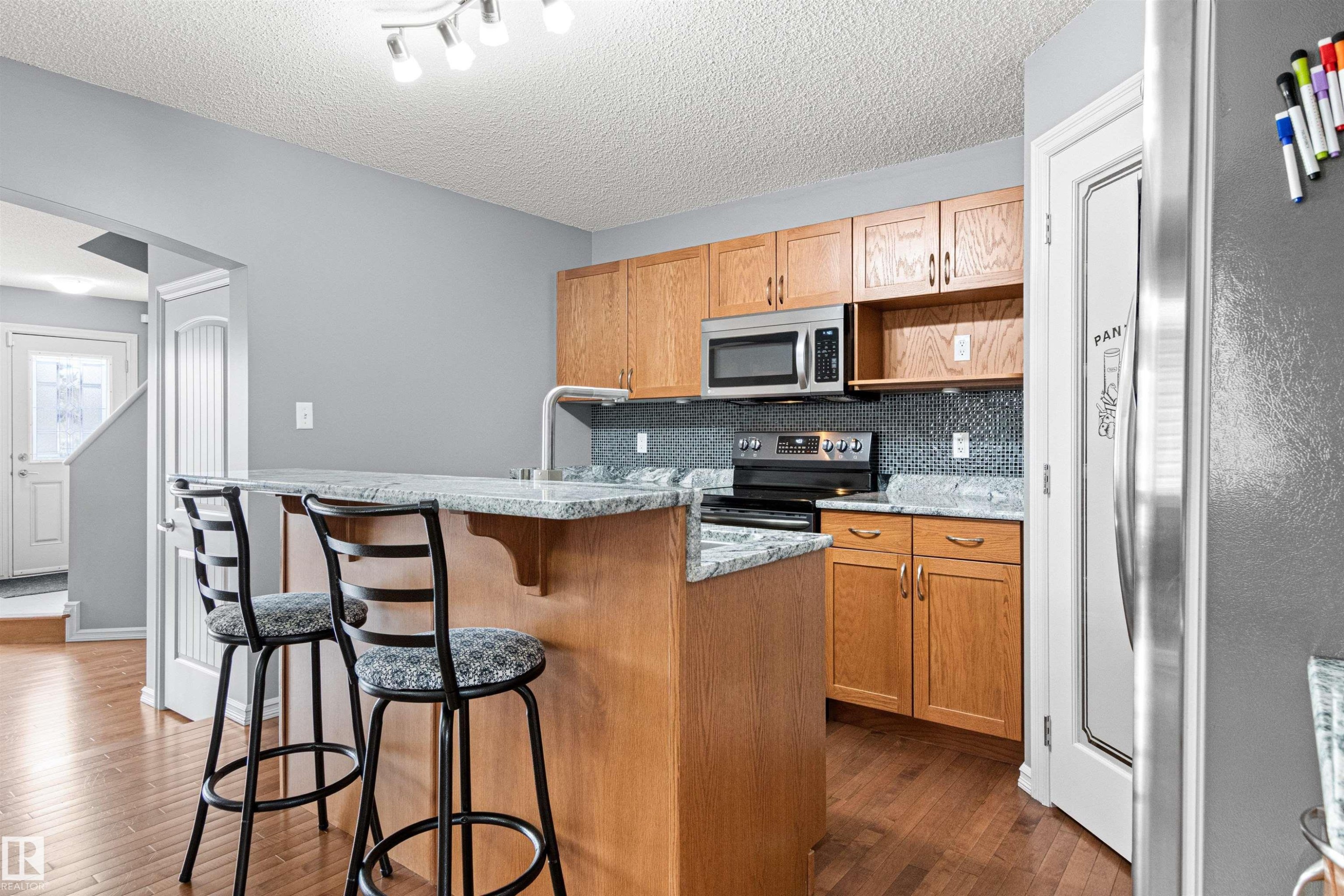Kitchen featuring wood-finish cabinetry, granite-style countertops, mosaic tile backsplash, stainless steel appliances, and a central island with an integrated breakfast bar - 1154 35A Avenue Nw, Edmonton, AB - Indoor Photo Showing Kitchen