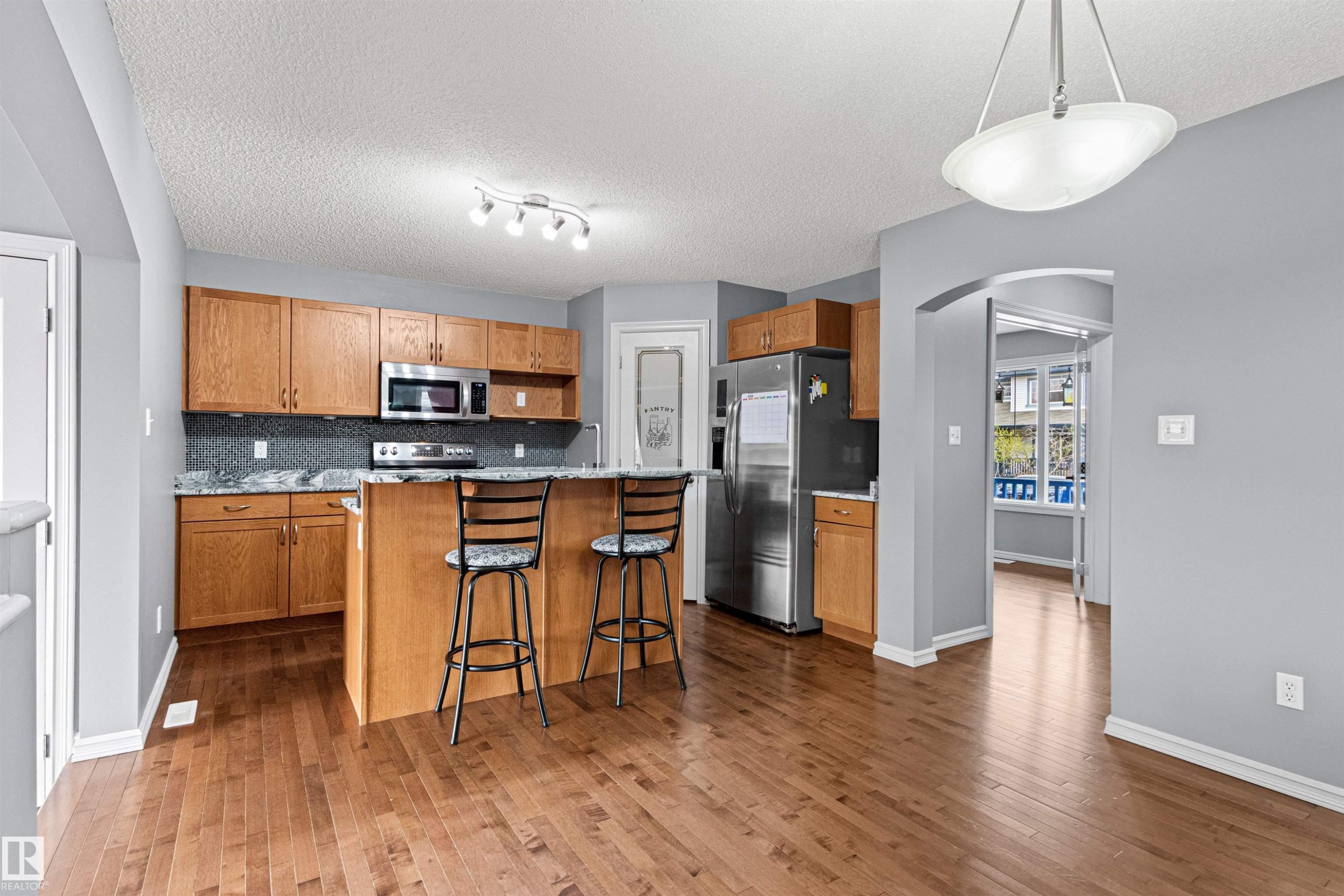 Open-concept kitchen featuring wood-finish cabinetry, stainless steel appliances, a breakfast bar, granite countertops, and a tiled backsplash - 1154 35A Avenue Nw, Edmonton, AB - Indoor Photo Showing Kitchen