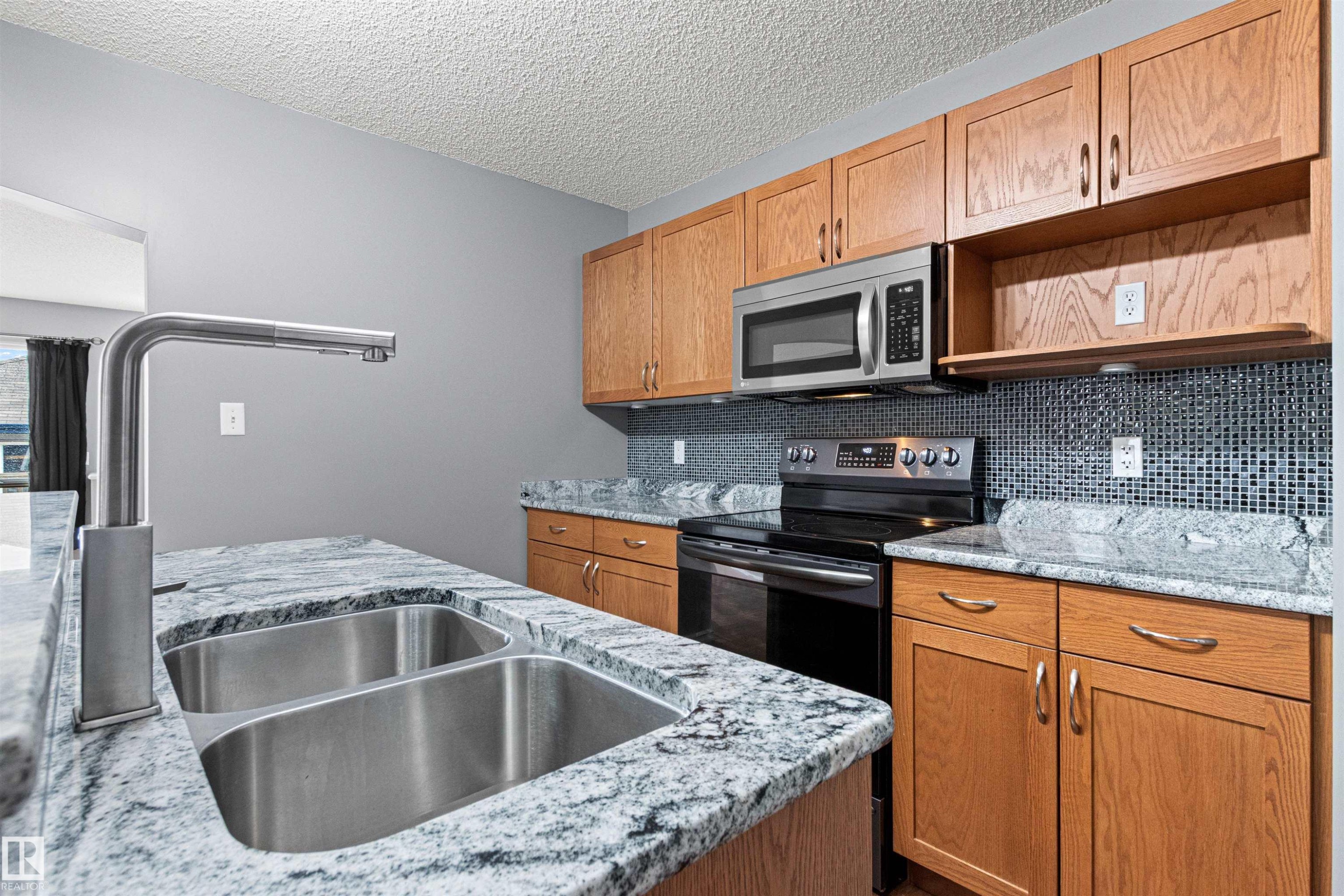 Kitchen featuring granite countertops, a double stainless steel sink with a modern faucet, wood cabinetry, and a mosaic tile backsplash - 1154 35A Avenue Nw, Edmonton, AB - Indoor Photo Showing Kitchen With Double Sink