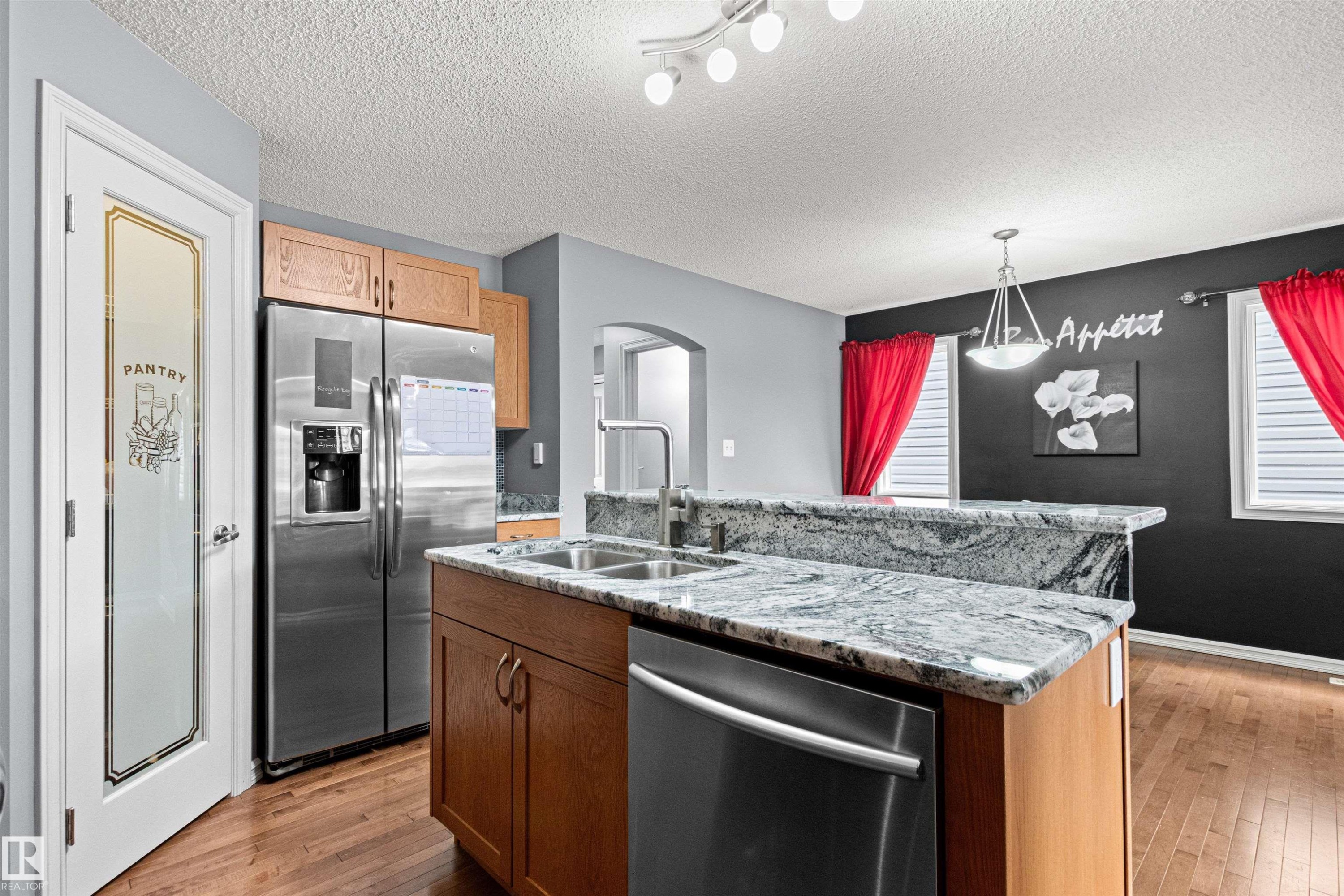 Kitchen featuring an island with a double basin sink, granite countertops, wood cabinetry, and stainless steel appliances - 1154 35A Avenue Nw, Edmonton, AB - Indoor Photo Showing Kitchen With Double Sink