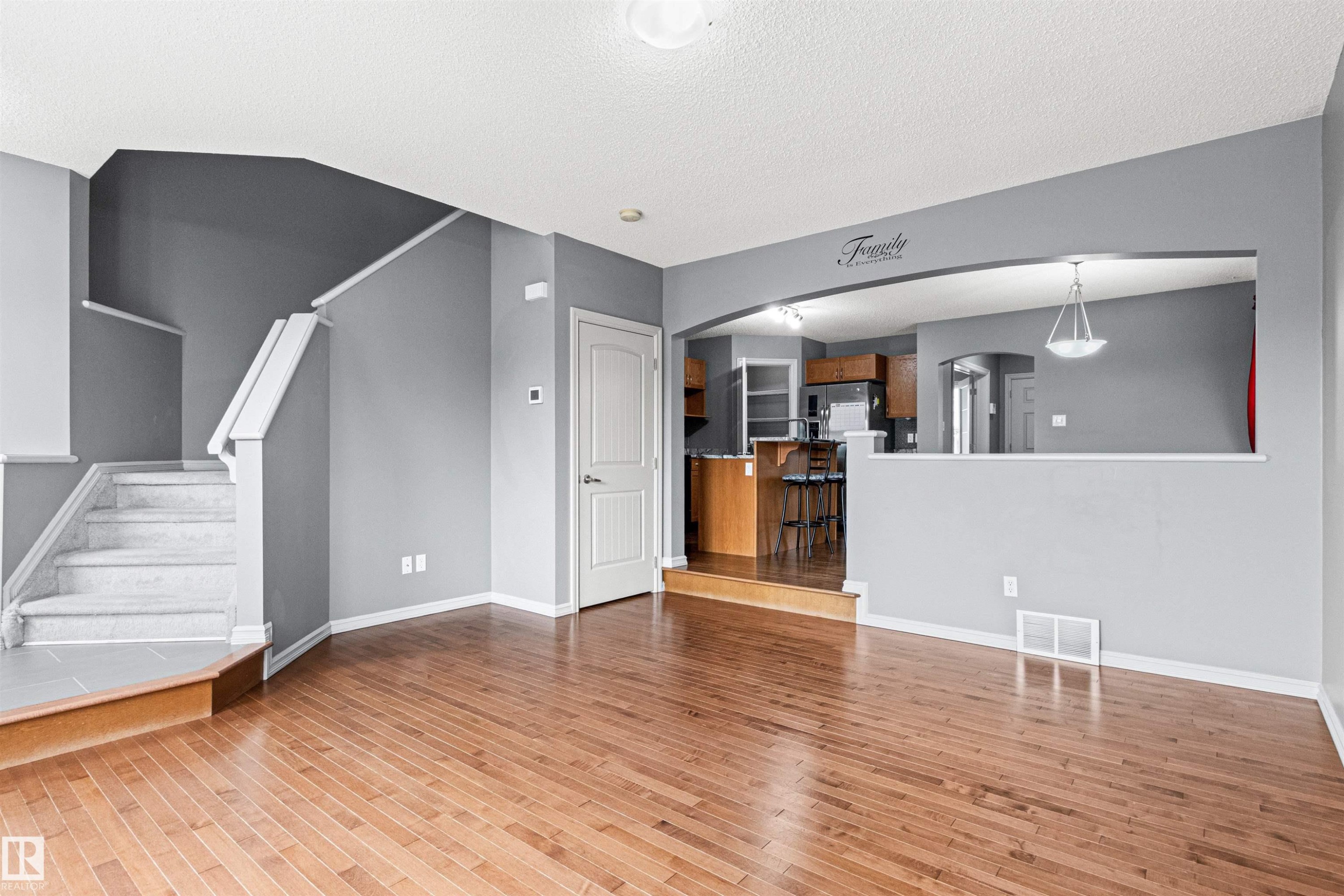 Spacious interior featuring wood-finish flooring, a carpeted staircase with white risers, and a functional half-wall with an arched opening - 1154 35A Avenue Nw, Edmonton, AB - Indoor Photo Showing Other Room