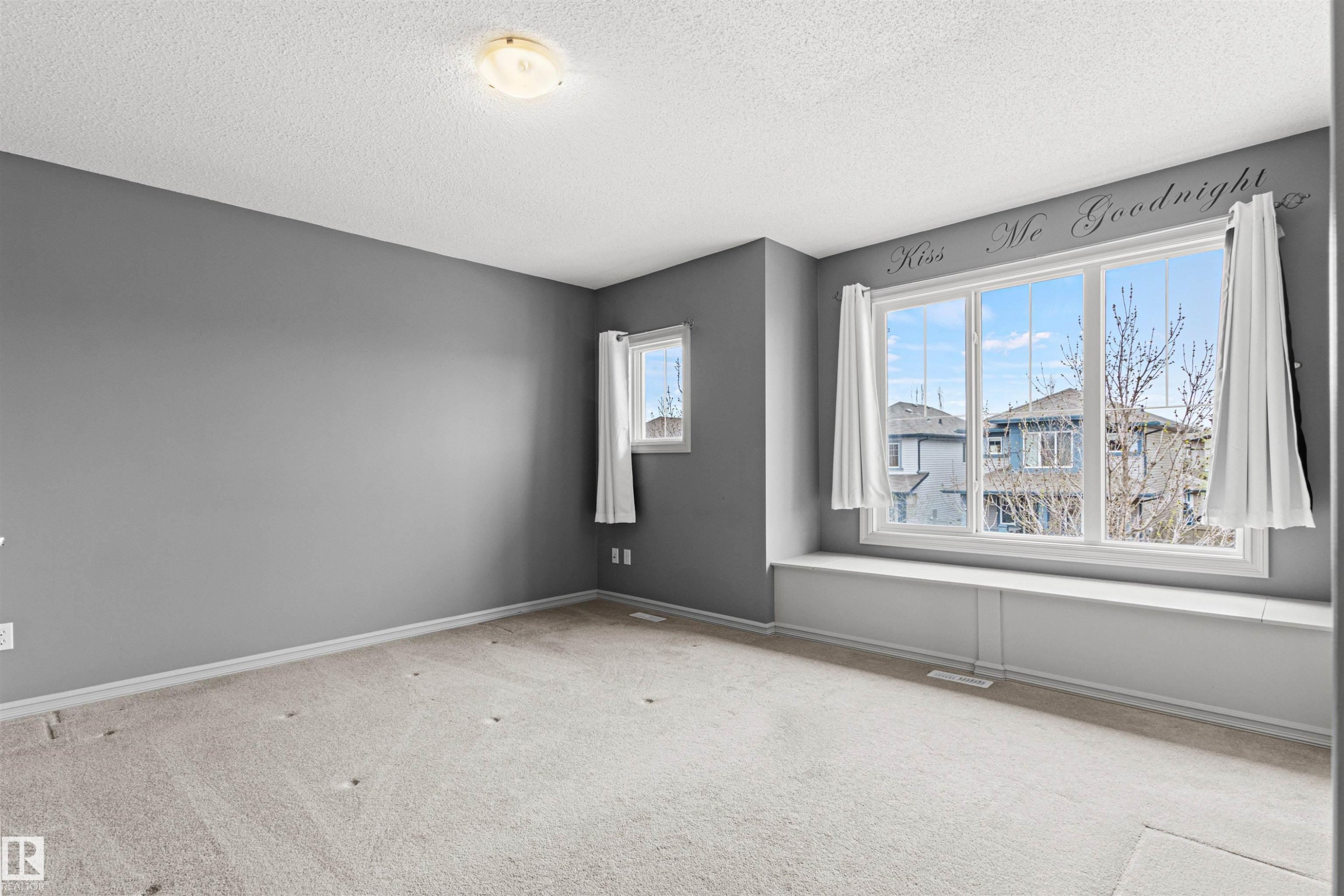 Carpeted interior room featuring a large window with a built-in window seat, a smaller casement window, gray wall paint, and a ceiling-mounted light fixture - 1154 35A Avenue Nw, Edmonton, AB - Indoor Photo Showing Other Room