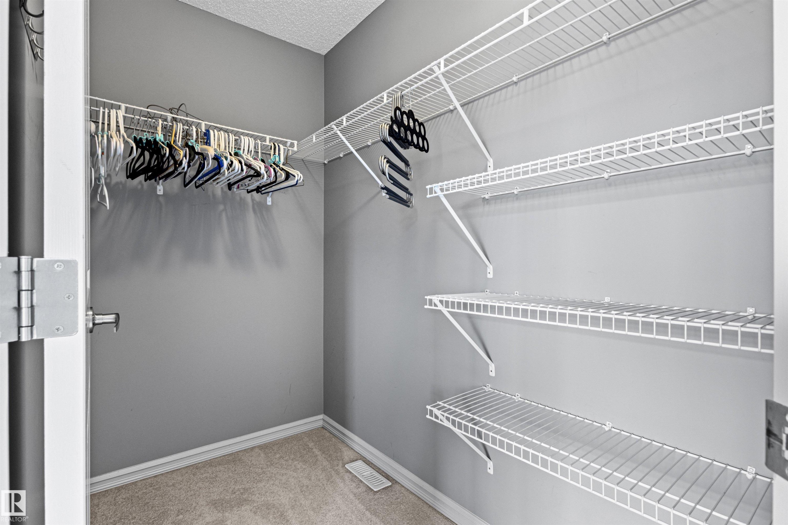 Walk-in closet featuring wire shelving, wire hanging rods, neutral gray wall paint, white trim, and light-toned carpet flooring - 1154 35A Avenue Nw, Edmonton, AB - Indoor With Storage