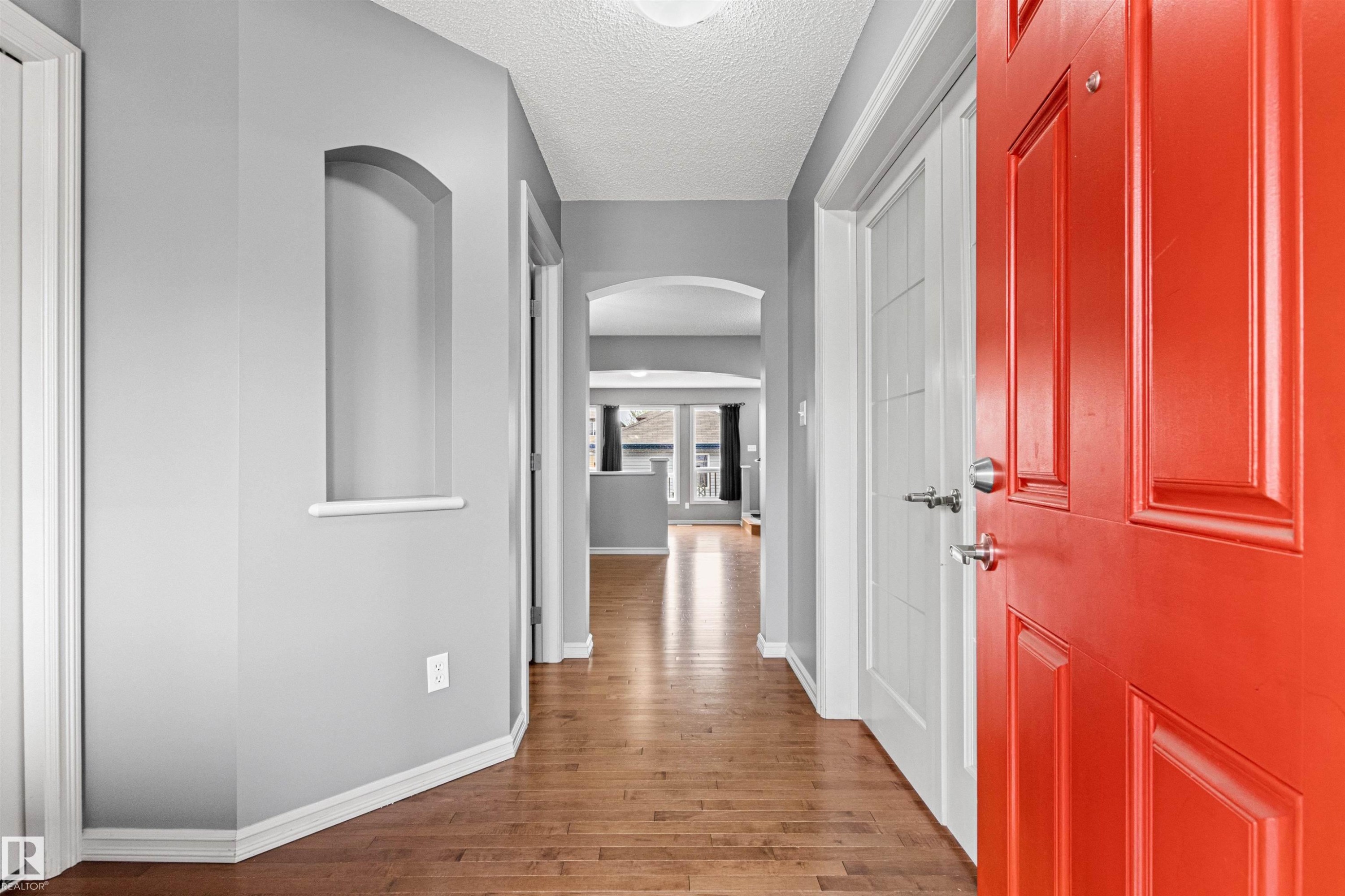 Entryway featuring a bright red panel door, wood-finish flooring, a decorative wall niche, and an arched hallway opening - 1154 35A Avenue Nw, Edmonton, AB - Indoor Photo Showing Other Room