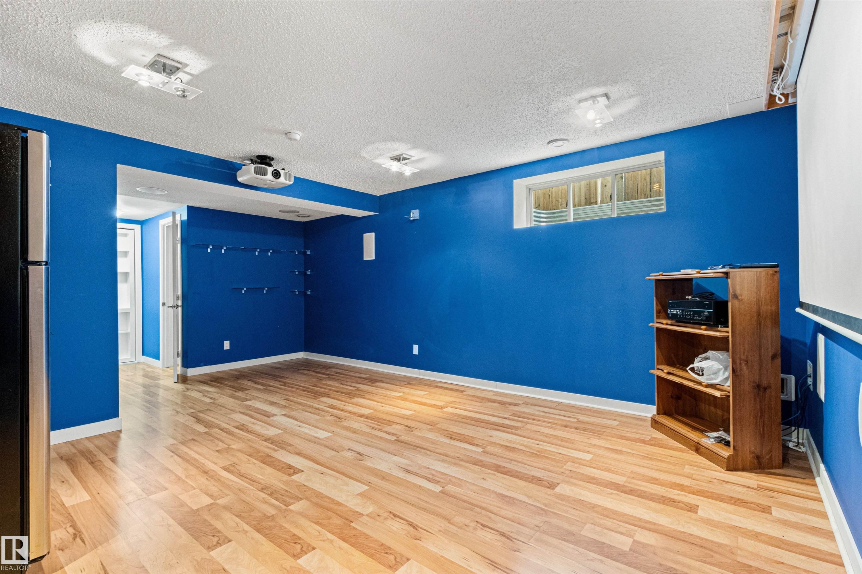 Finished lower level featuring recessed lighting, wood-finish flooring, a wall-mounted projector, and a window well - 1154 35A Avenue Nw, Edmonton, AB - Indoor Photo Showing Other Room