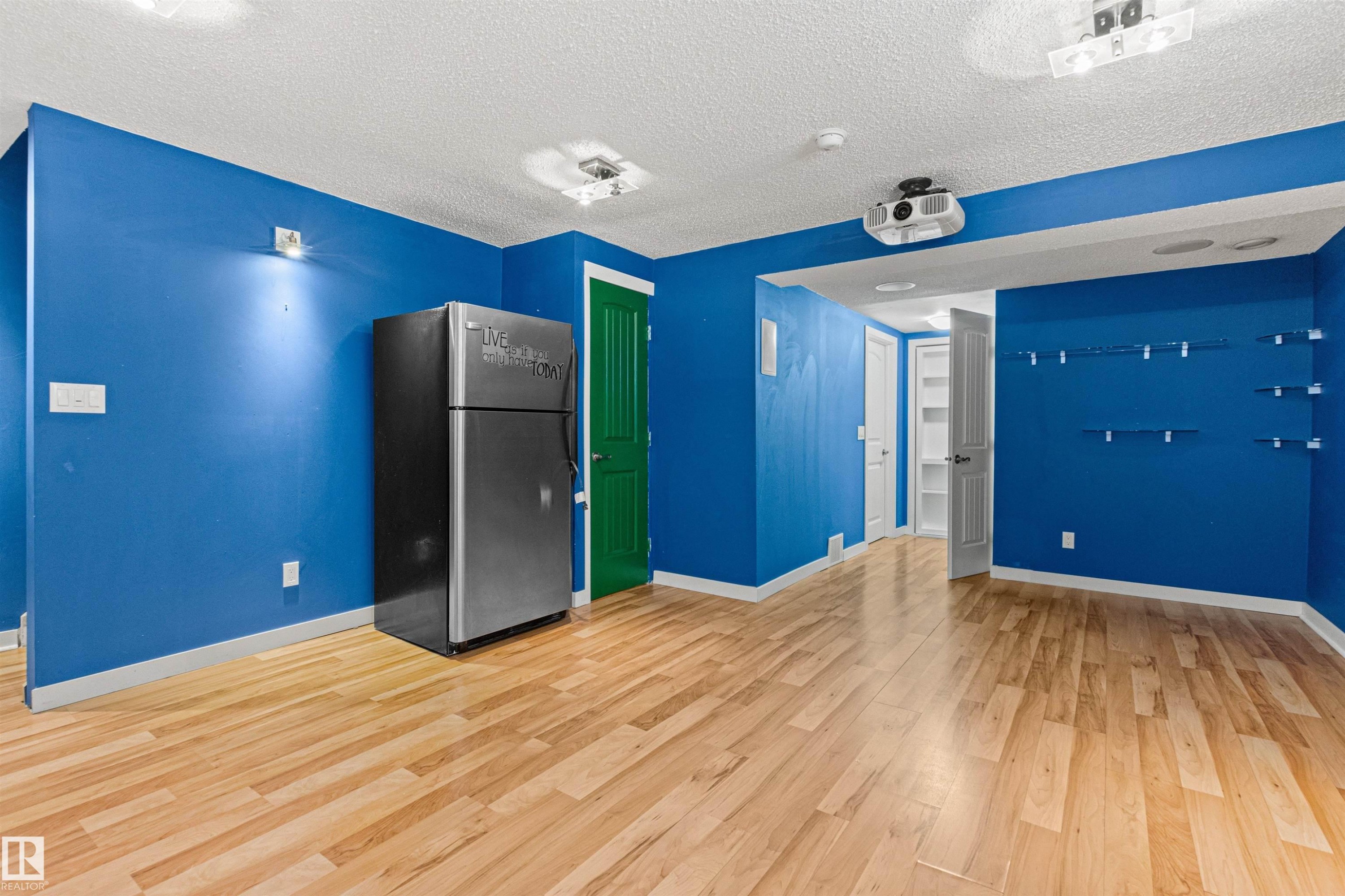 Spacious room featuring wood-finish flooring, vibrant blue walls, and a recessed ceiling projector - 1154 35A Avenue Nw, Edmonton, AB - Indoor Photo Showing Other Room