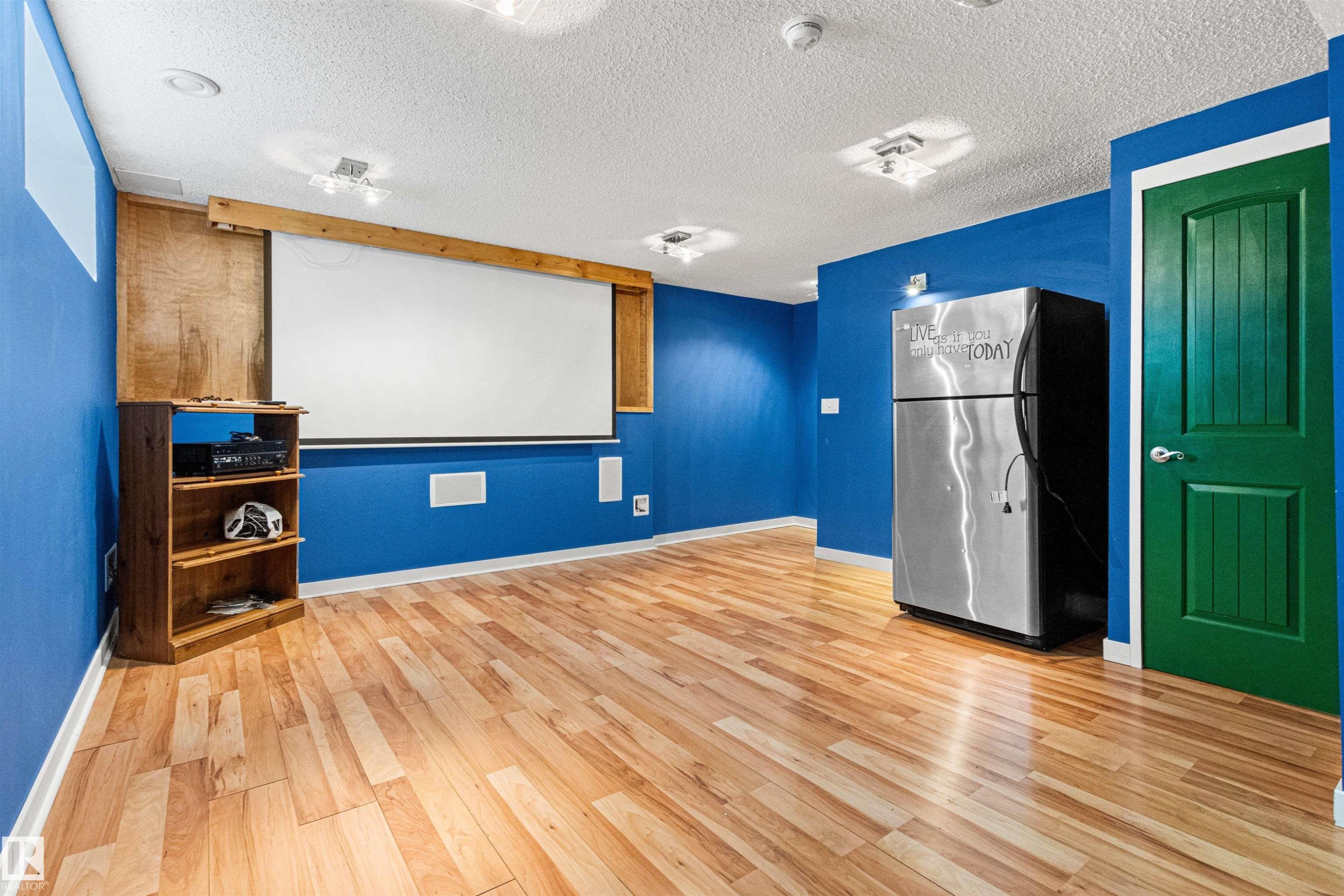 Spacious recreation room featuring wood-finish flooring, a built-in projector screen, recessed lighting, and a vibrant green door - 1154 35A Avenue Nw, Edmonton, AB - Indoor Photo Showing Other Room