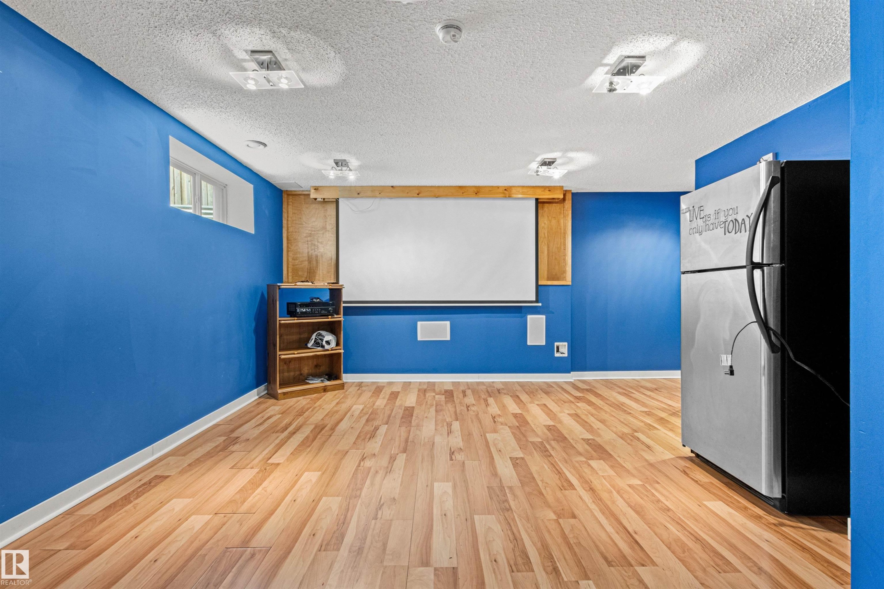 Spacious room featuring wood-finish flooring, a mounted projection screen, integrated audio speakers, a high window, and ample recessed lighting - 1154 35A Avenue Nw, Edmonton, AB - Indoor Photo Showing Other Room