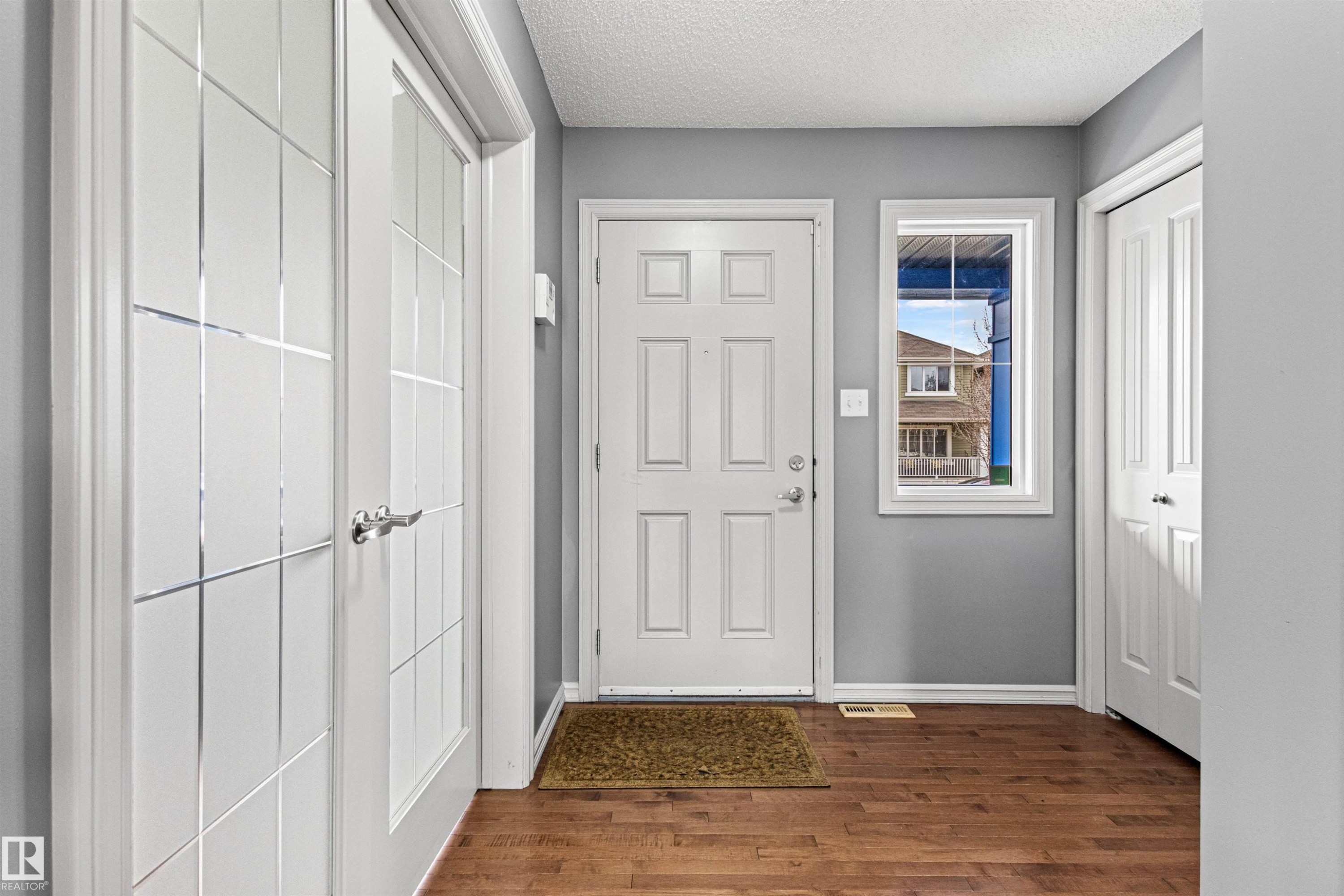 Entryway featuring a white paneled front door, wood-finish flooring, a rectangular window, and two closet doors - 1154 35A Avenue Nw, Edmonton, AB - Indoor Photo Showing Other Room