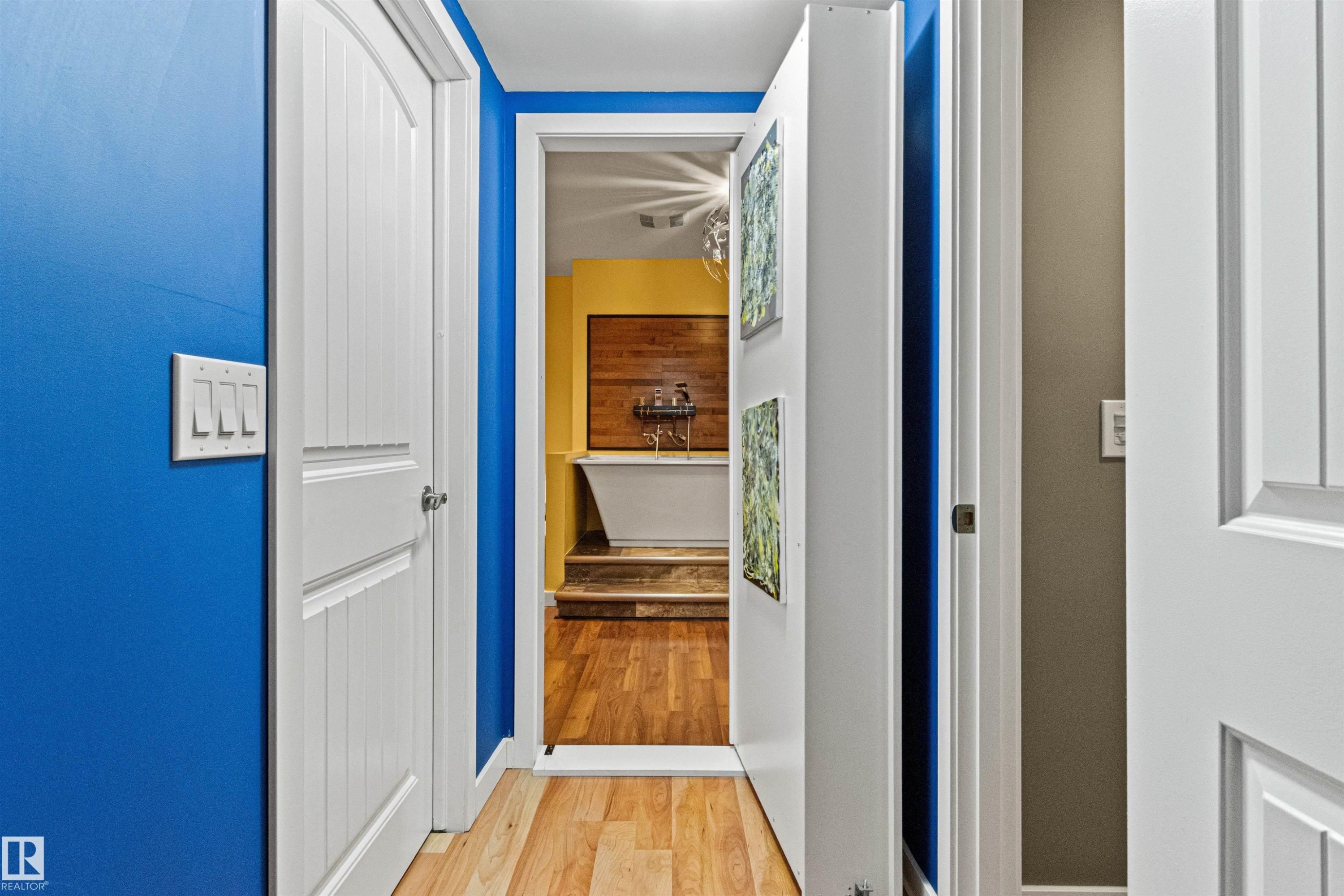 Hallway featuring light wood-finish flooring, white paneled doors, and a bright blue accent wall - 1154 35A Avenue Nw, Edmonton, AB - Indoor Photo Showing Other Room