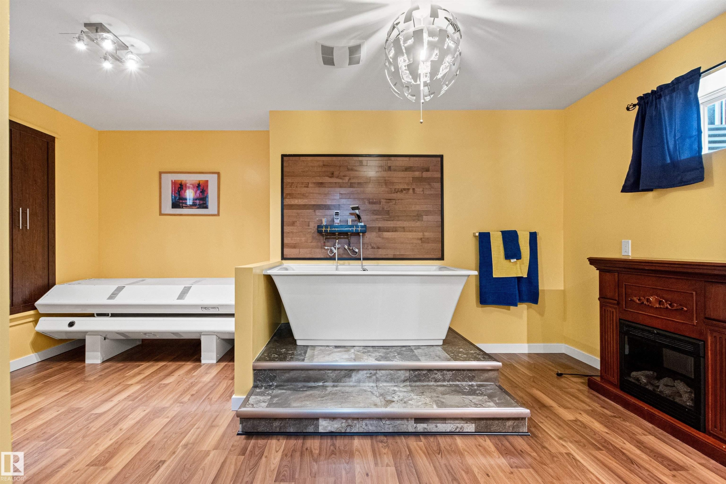 Freestanding soaking tub on a raised tile platform with a wood-paneled accent wall - 1154 35A Avenue Nw, Edmonton, AB - Indoor With Fireplace