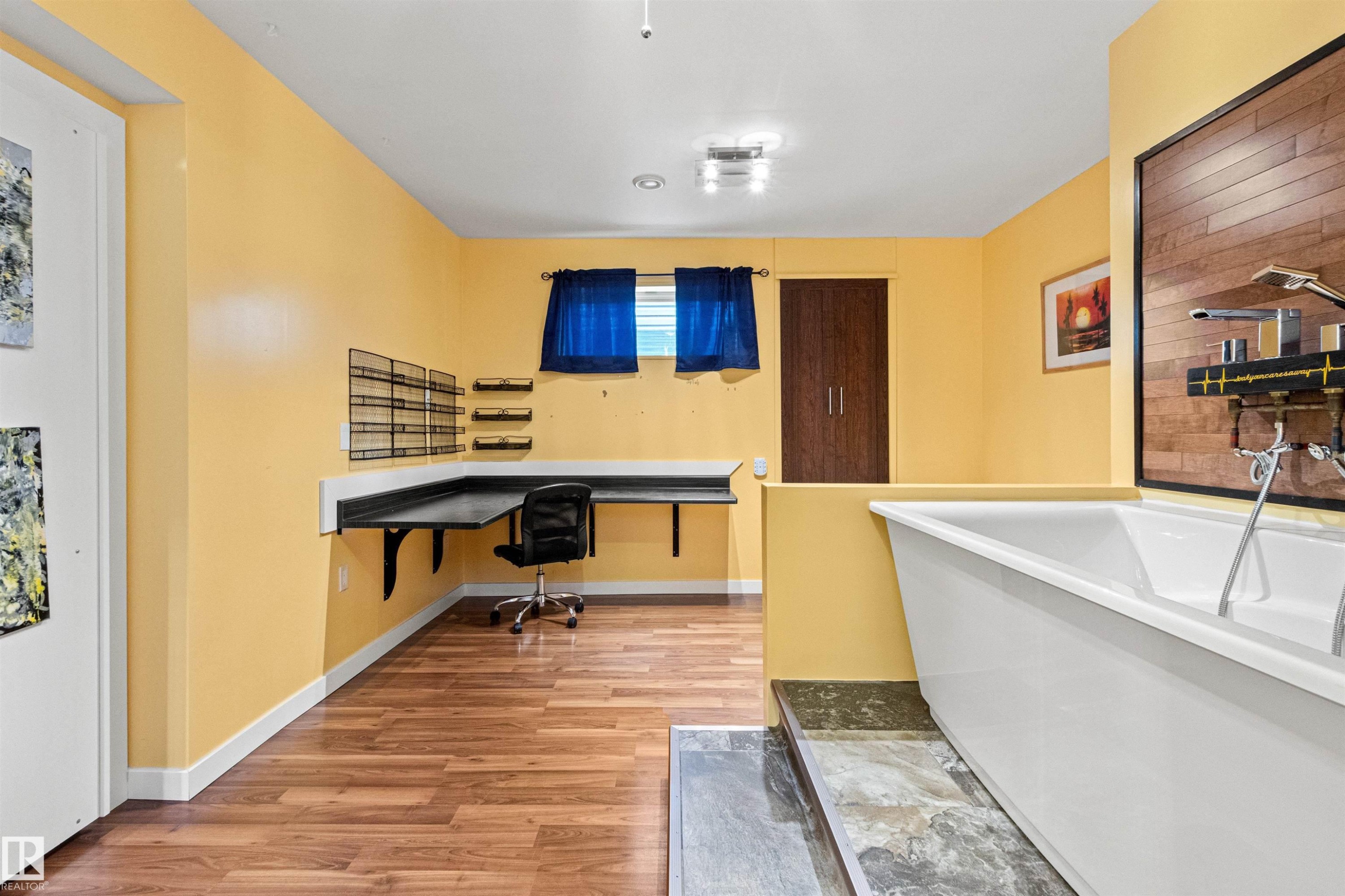 Spacious lower-level area featuring wood-finish flooring, a built-in corner desk, and a freestanding soaking tub - 1154 35A Avenue Nw, Edmonton, AB - Indoor