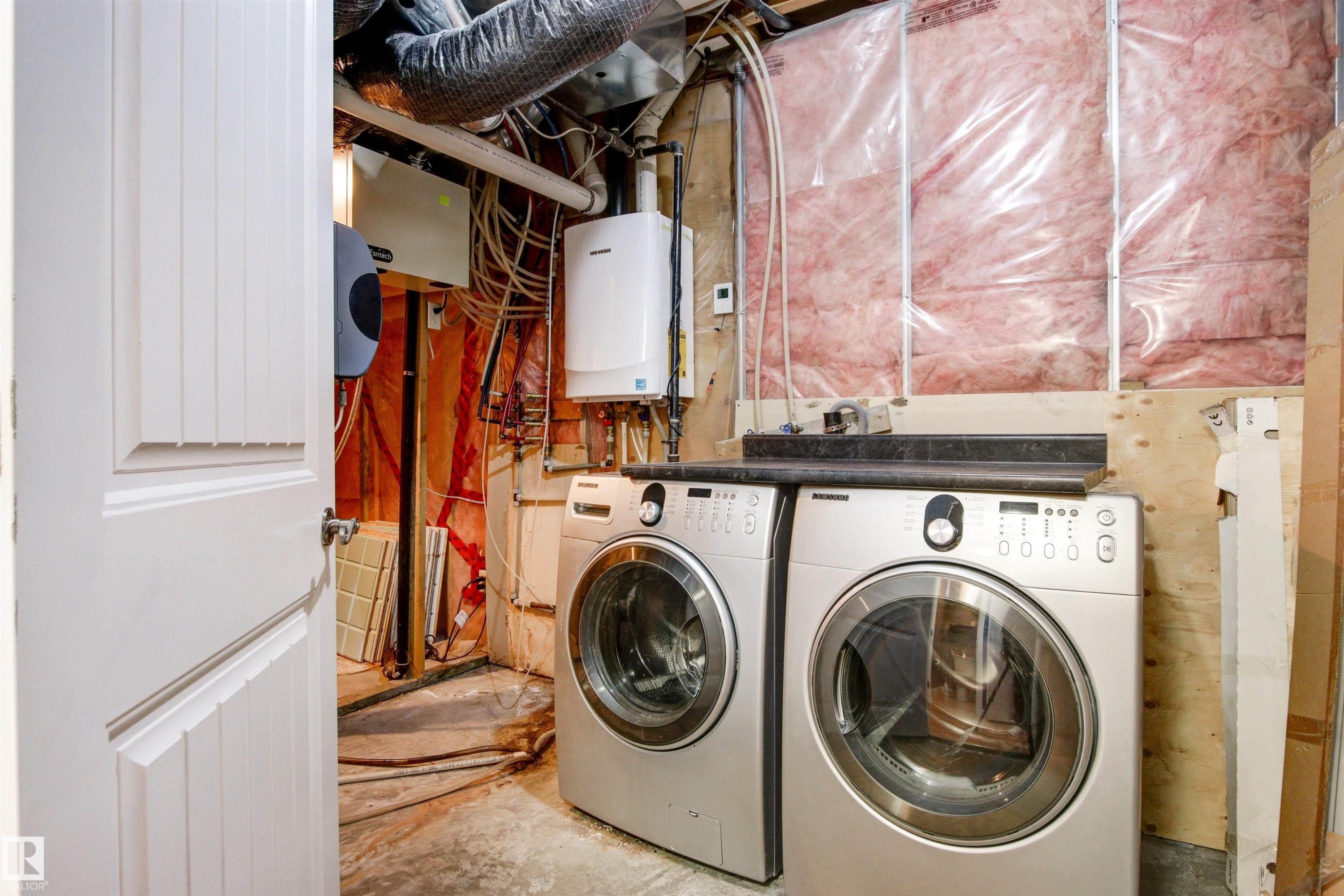 Laundry area featuring a stackable washer and dryer set, a utility sink, and exposed insulation - 1154 35A Avenue Nw, Edmonton, AB - Indoor Photo Showing Laundry Room
