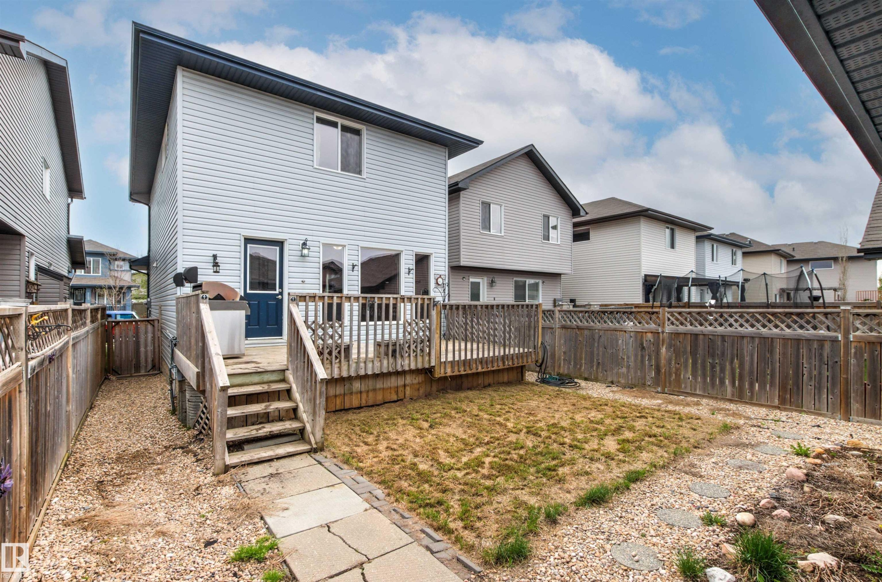 Rear exterior featuring light-toned horizontal siding, a private wooden deck with railings, and an egress door with a dark blue finish - 1154 35A Avenue Nw, Edmonton, AB - Outdoor With Deck Patio Veranda With Exterior