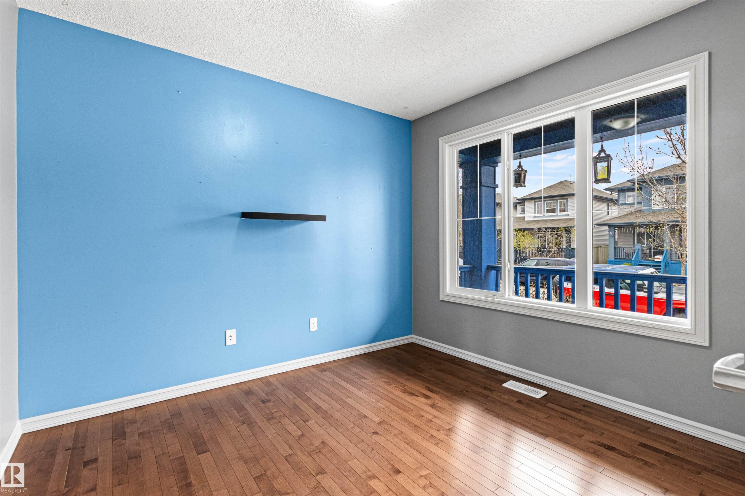 Bright room featuring wood-finish flooring, a large multi-pane window, and a light blue accent wall - 1154 35A Avenue Nw, Edmonton, AB - Indoor Photo Showing Other Room