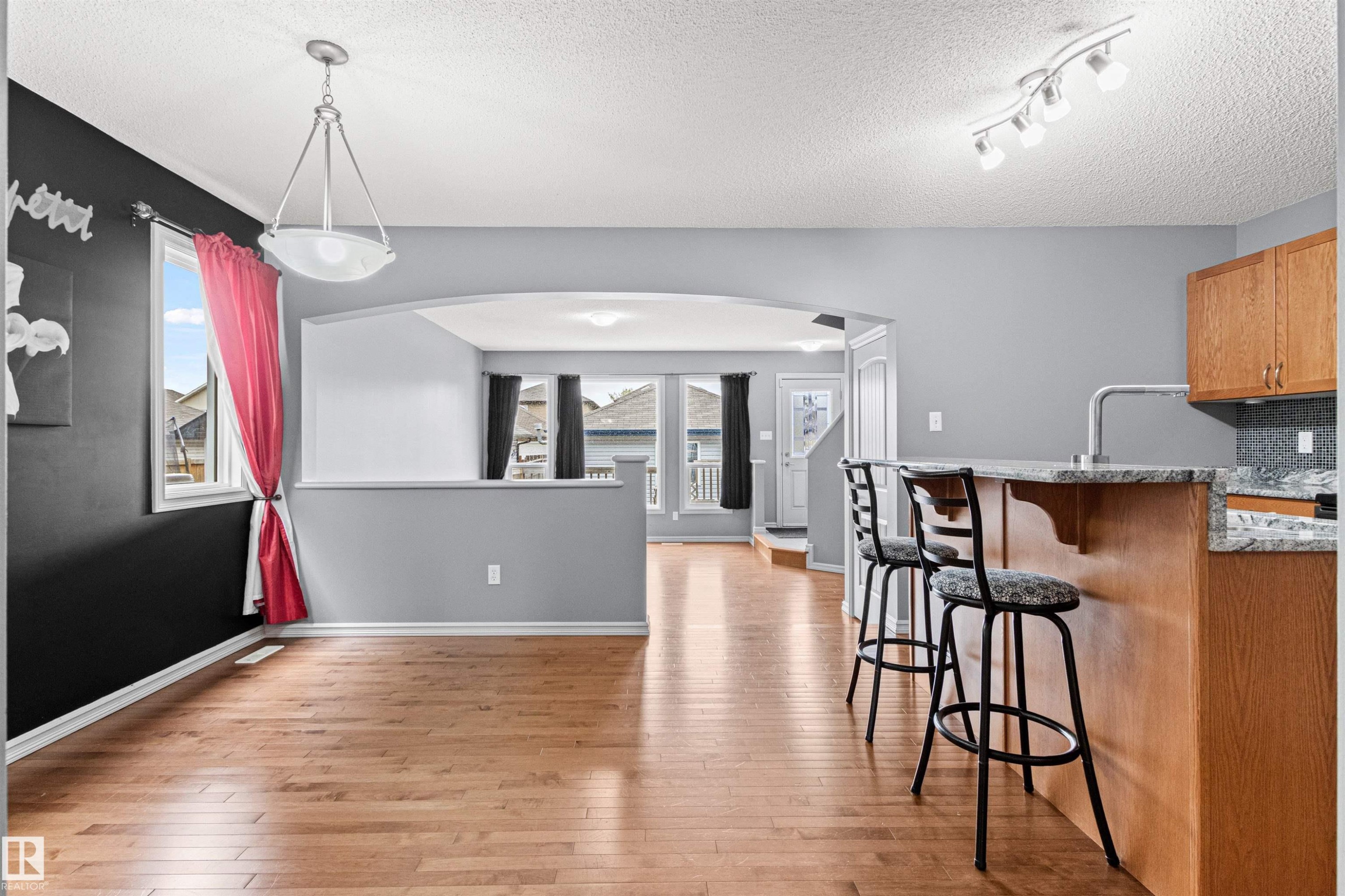 Open-concept living area featuring wood-finish flooring, a kitchen island with seating, a pendant light fixture, track lighting, and an arched doorway - 1154 35A Avenue Nw, Edmonton, AB - Indoor Photo Showing Kitchen