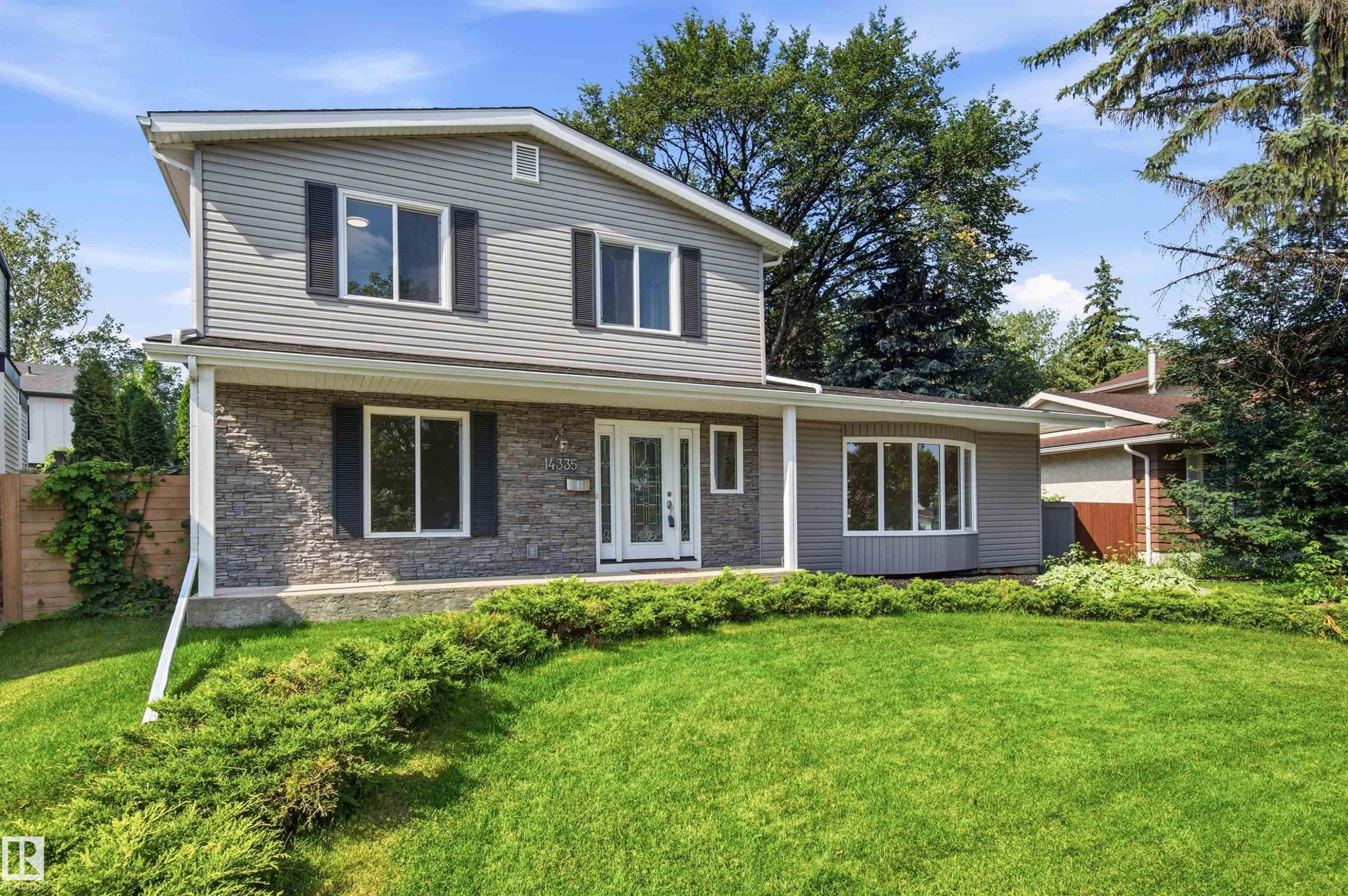 Two-story residence featuring gray siding, stone facade accents, a covered front porch, and a bay window - 14335 47 Avenue Nw, Edmonton, AB - Outdoor