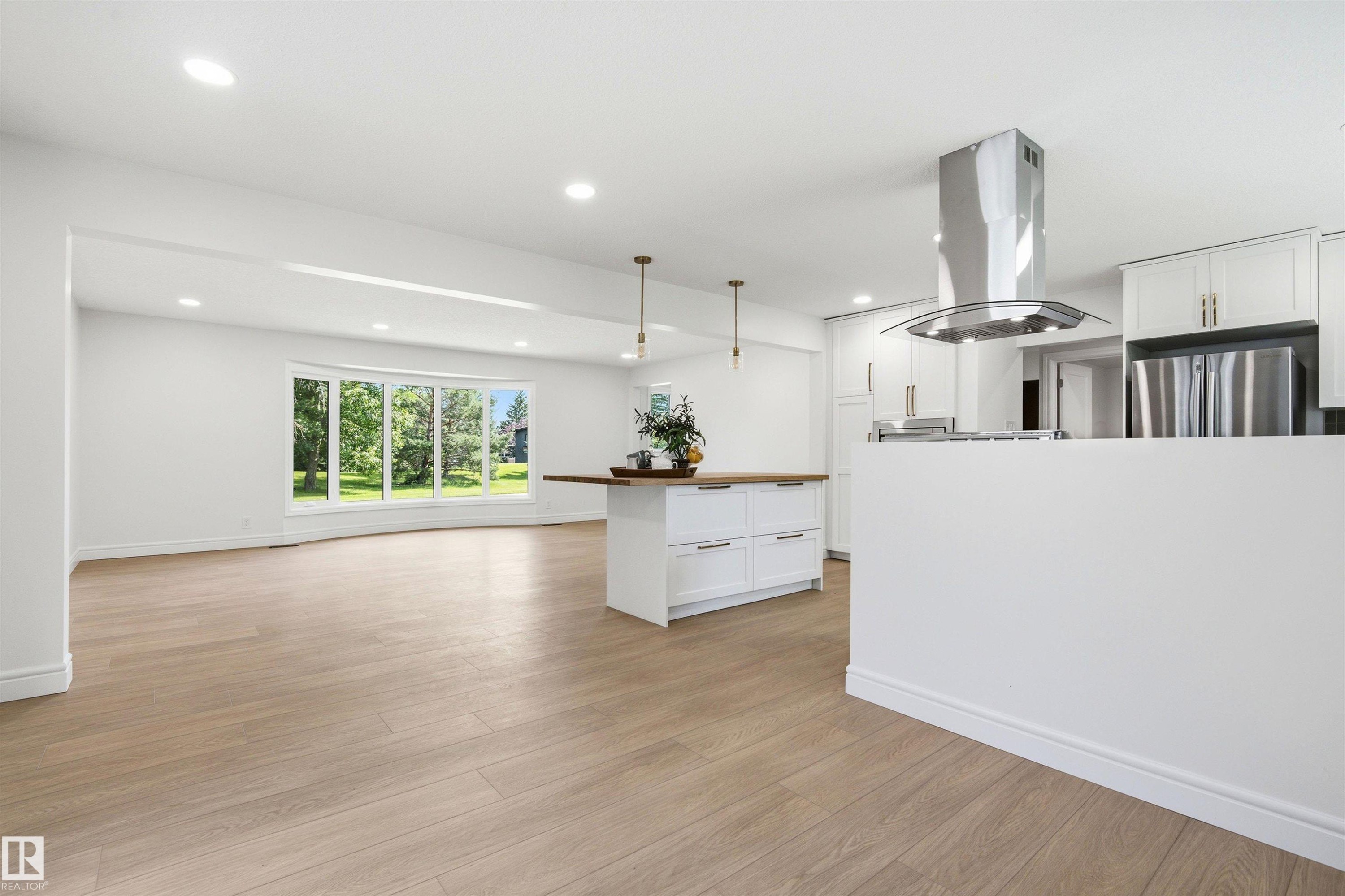 Open-concept living space featuring wood-finish flooring, recessed lighting, and a kitchen with white cabinetry and stainless steel appliances - 14335 47 Avenue Nw, Edmonton, AB - Indoor