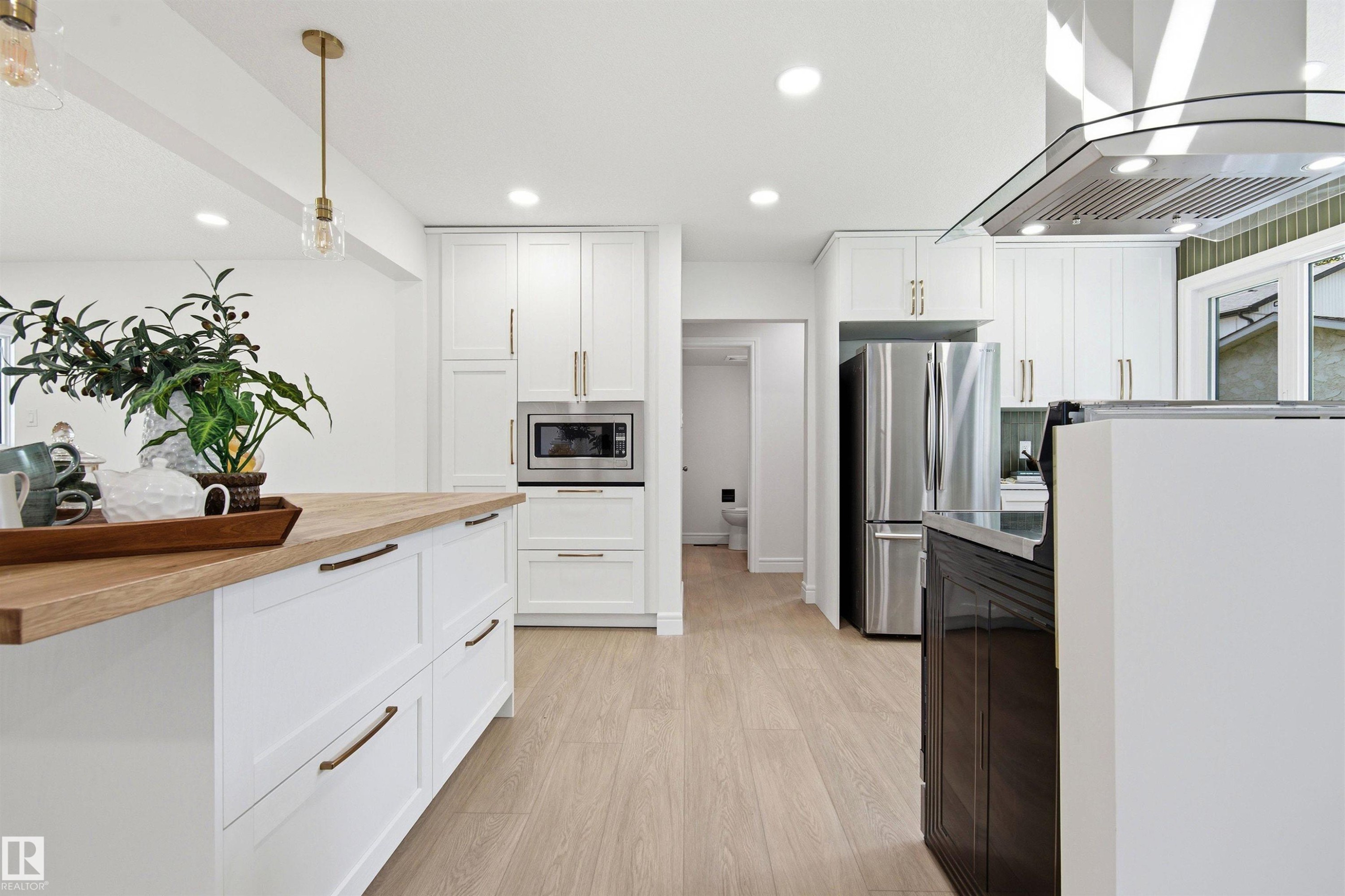 Modern kitchen featuring white shaker cabinetry, stainless steel appliances, a range hood, and light wood-finish flooring - 14335 47 Avenue Nw, Edmonton, AB - Indoor Photo Showing Kitchen With Upgraded Kitchen