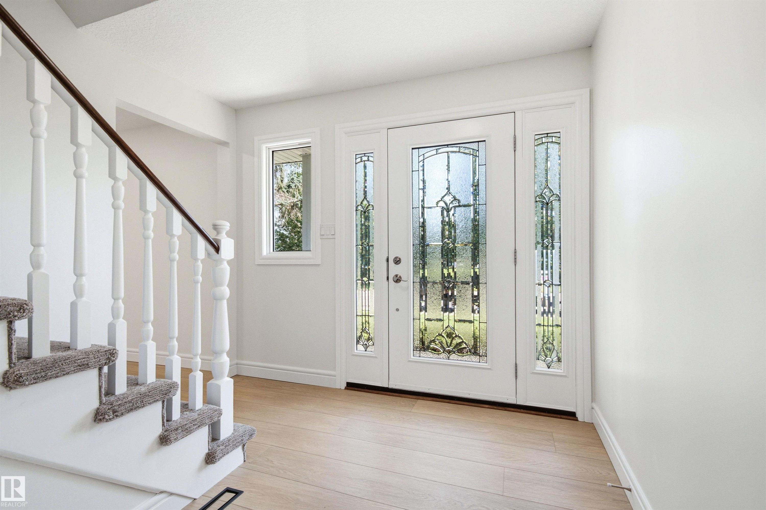 Foyer featuring a decorative glass panel entry door with matching sidelites, light wood-finish flooring, and a white staircase with a dark wood handrail - 14335 47 Avenue Nw, Edmonton, AB - Indoor Photo Showing Other Room