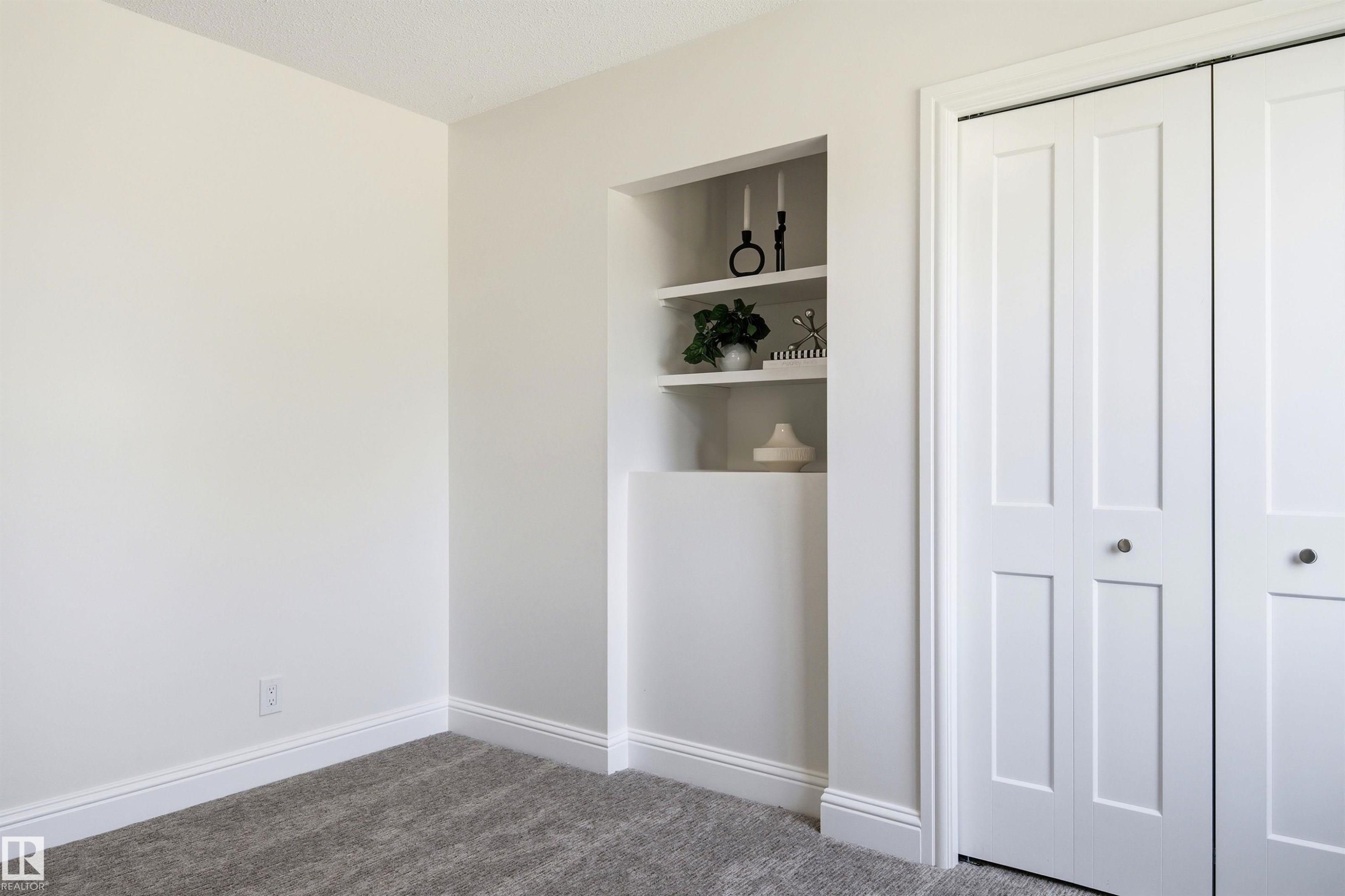 Recessed shelving unit featuring three display shelves, adjacent to a bi-fold closet with two paneled doors and round knobs - 14335 47 Avenue Nw, Edmonton, AB - Indoor Photo Showing Other Room