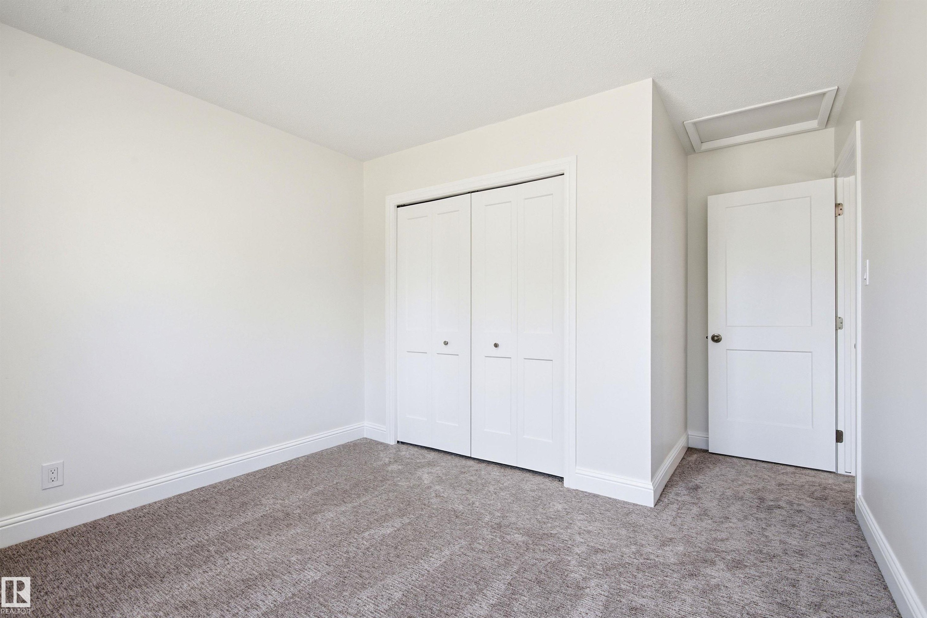 Neutral wall colors, plush carpet flooring, white baseboards, white bi-fold closet doors, and white interior door - 14335 47 Avenue Nw, Edmonton, AB - Indoor Photo Showing Other Room