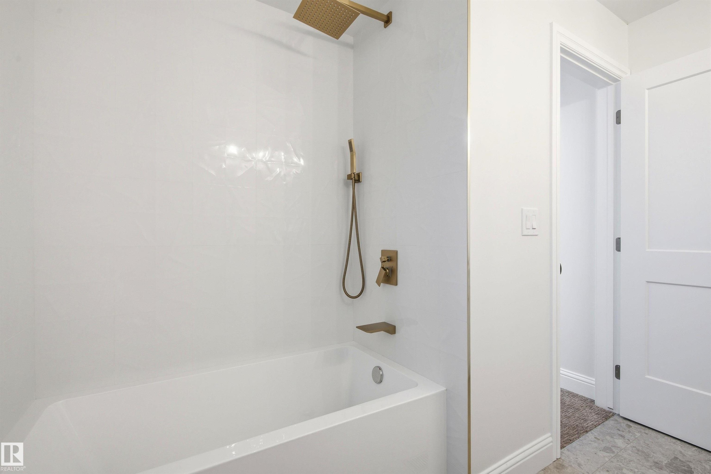 White bathtub and shower surround featuring a brass-finish rainfall shower head, handheld shower, and tub spout - 14335 47 Avenue Nw, Edmonton, AB - Indoor Photo Showing Bathroom