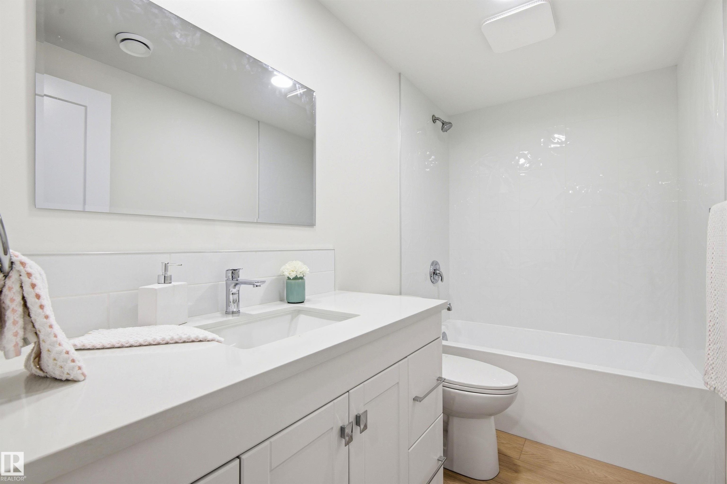 Bathroom featuring a white vanity with an integrated sink, chrome faucet, and a large wall-mounted mirror - 14335 47 Avenue Nw, Edmonton, AB - Indoor Photo Showing Bathroom