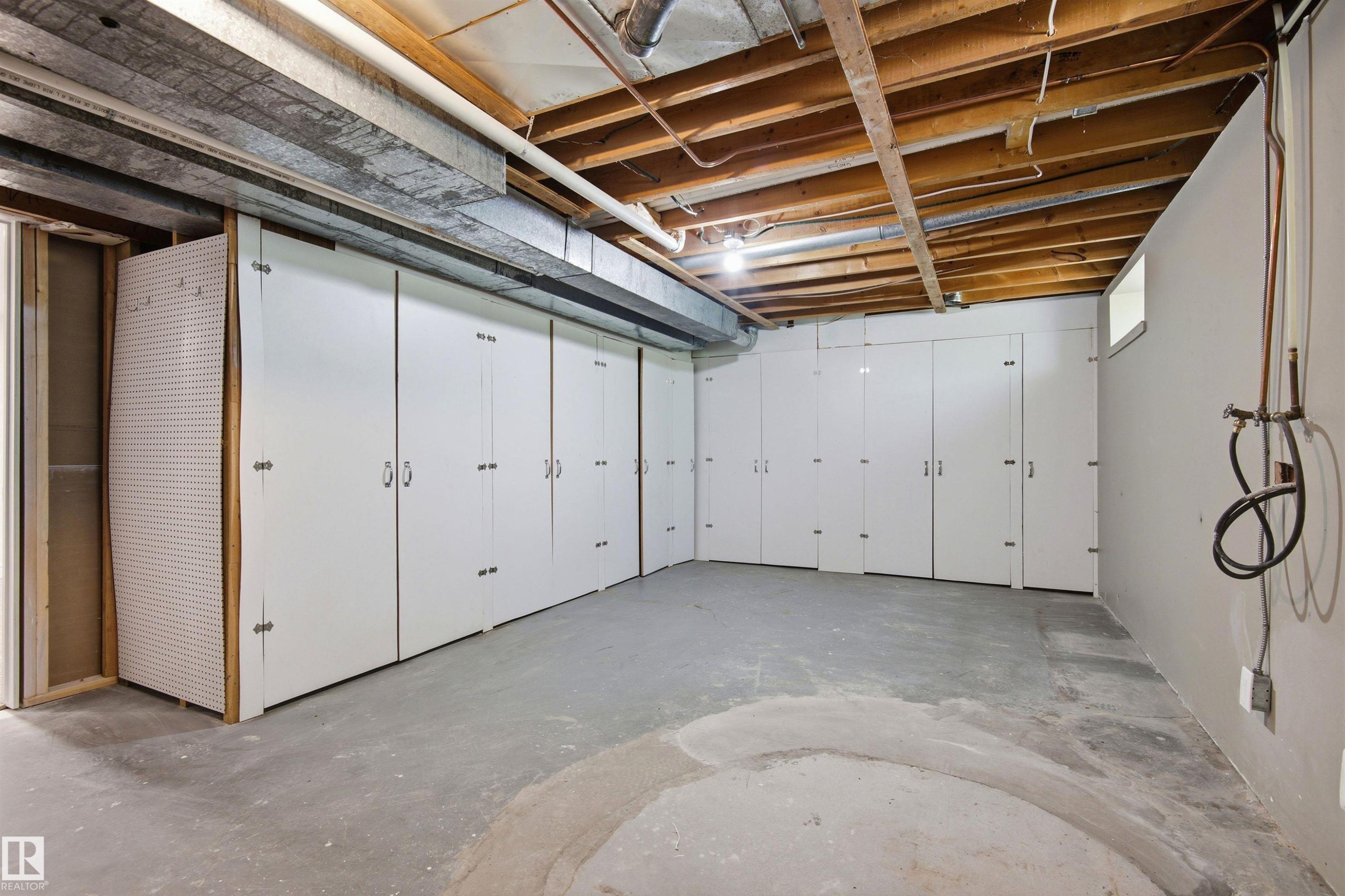 Basement storage area featuring extensive built-in white cabinetry with silver-toned hardware, exposed ceiling joists, and a concrete floor - 14335 47 Avenue Nw, Edmonton, AB - Indoor Photo Showing Garage