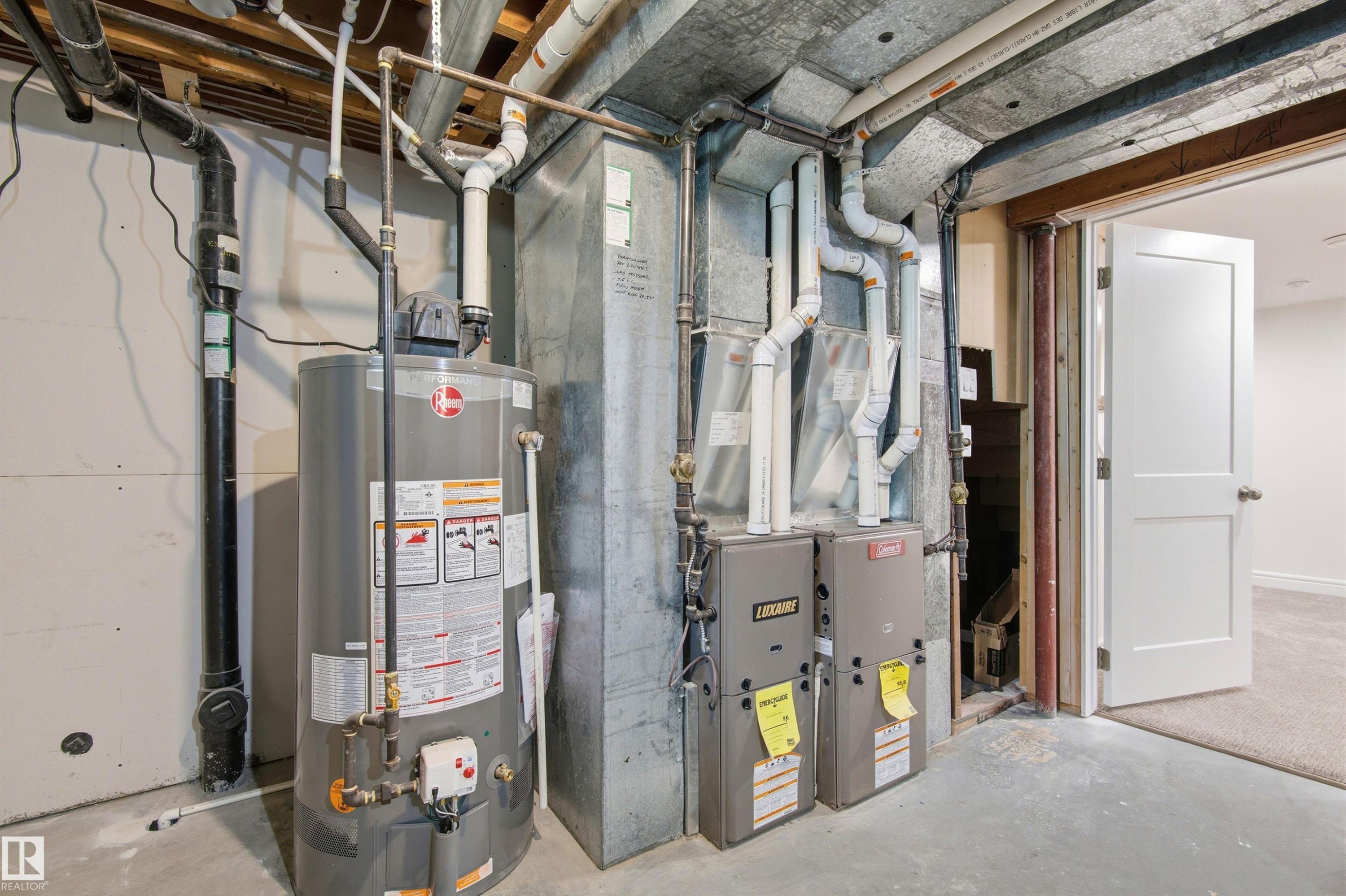 Basement utility area featuring a water heater, dual furnaces, exposed ductwork, and concrete flooring - 14335 47 Avenue Nw, Edmonton, AB - Indoor Photo Showing Basement