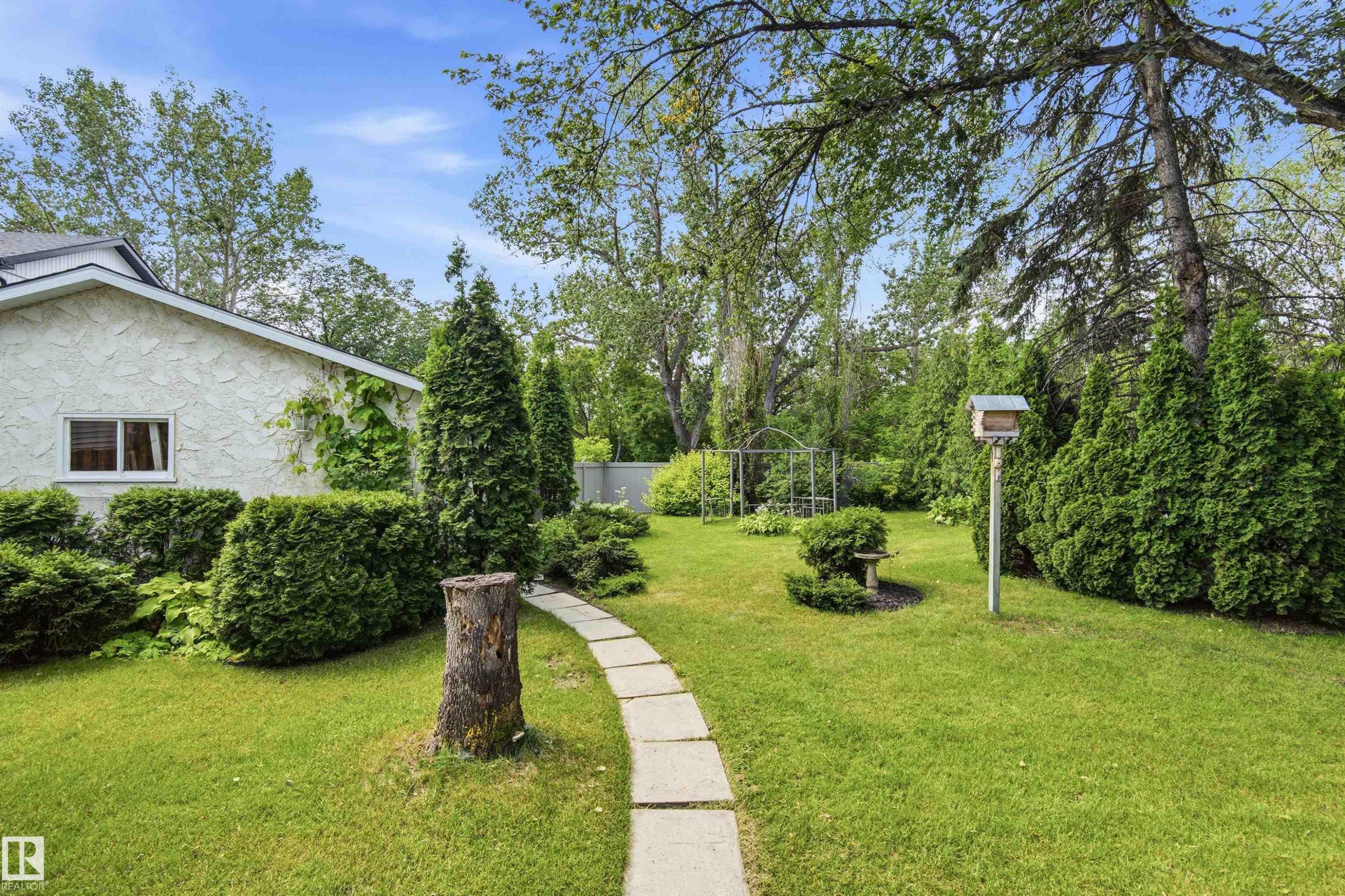 Expansive lawn area featuring a stone paver pathway, mature trees, and established shrubs - 14335 47 Avenue Nw, Edmonton, AB - Outdoor