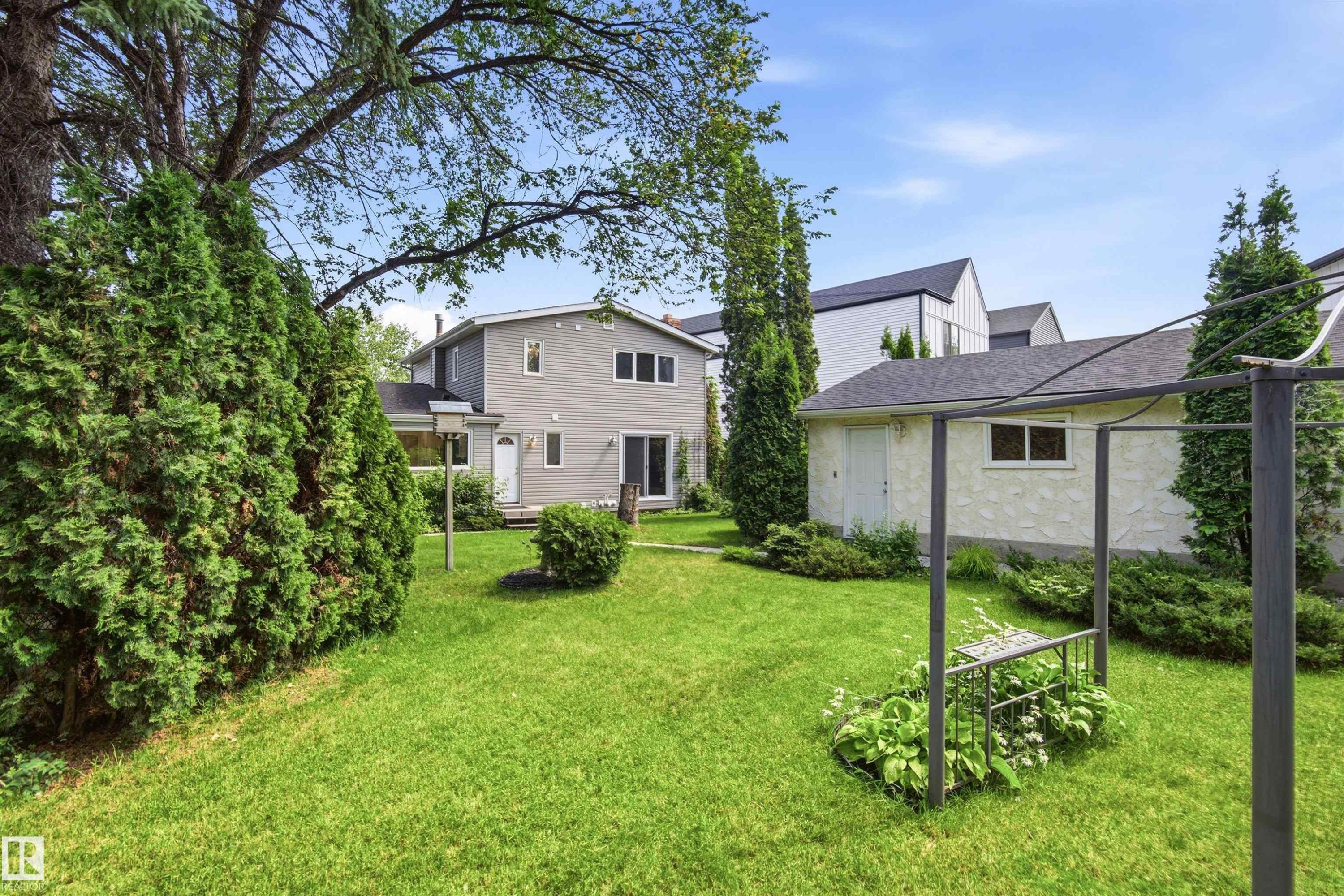 Expansive backyard with a manicured lawn, established perimeter plantings, and mature trees - 14335 47 Avenue Nw, Edmonton, AB - Outdoor